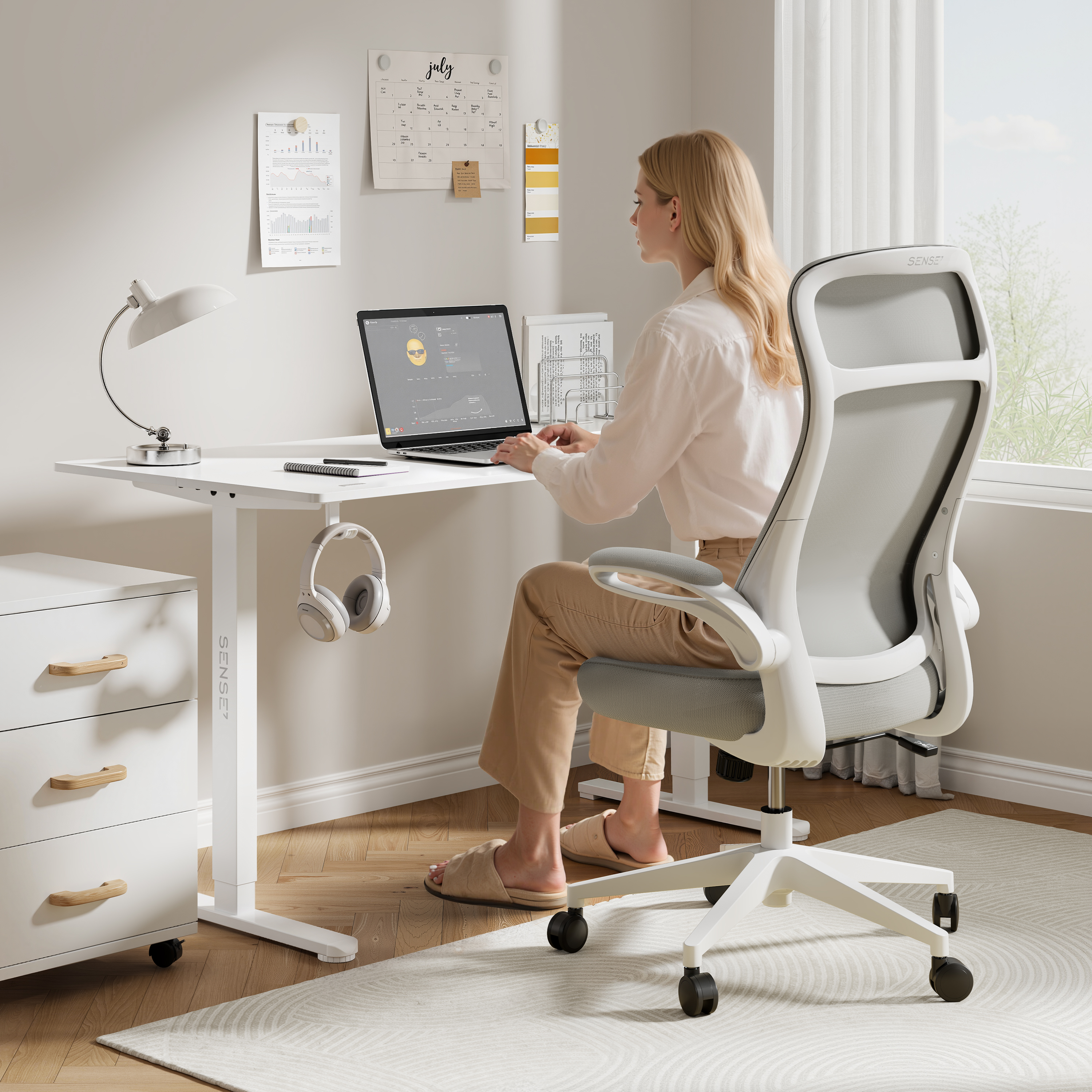 Vrouw aan een witte bureau met een laptop. Grijze stoel, witte lades, koptelefoon en bureaulamp. Kalender aan de muur.