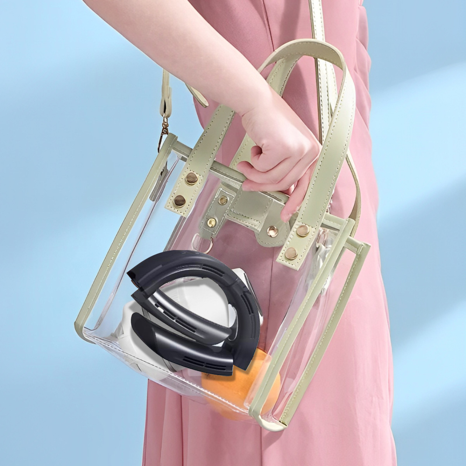 Eine Person hält eine transparente Tragetasche mit einem schwarzen Ventilator, einem weißen Gegenstand und einem orangefarbenen Gegenstand.