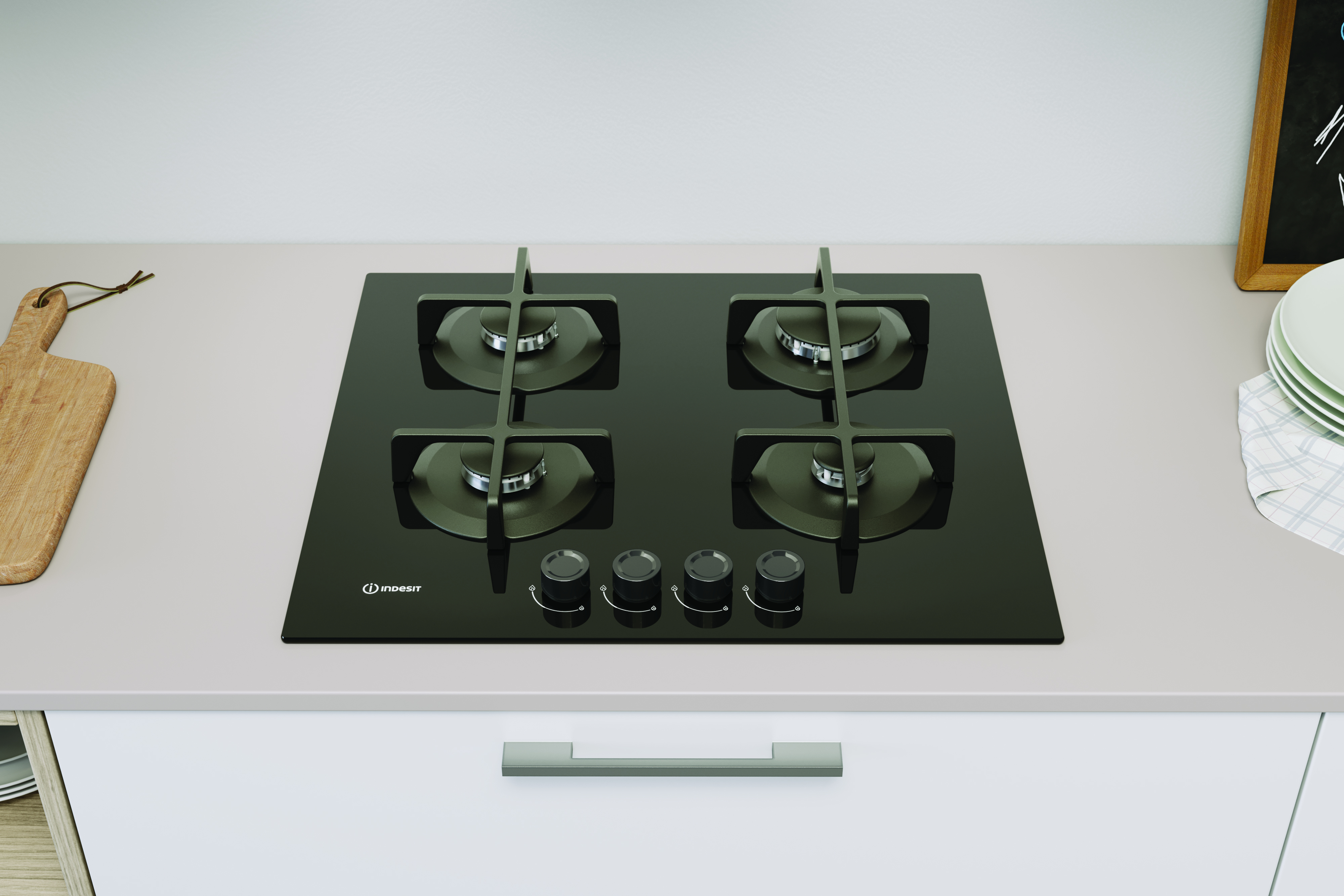 Czarna płyta grzewcza ze szklanym blatem, z czterema palnikami, pokrętłami i logo Indesit. W pobliżu deska drewniana i talerze.