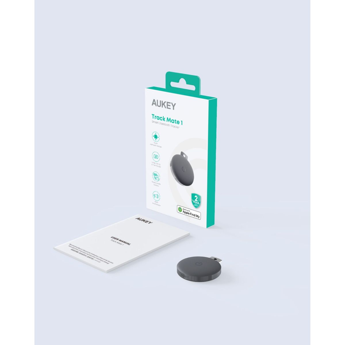 Eine weiße Schachtel mit dem Text 'AUKEY Track Mate 1' und einem grauen Tracker. Ein Benutzerhandbuch und der Tracker liegen auf dem Tisch.