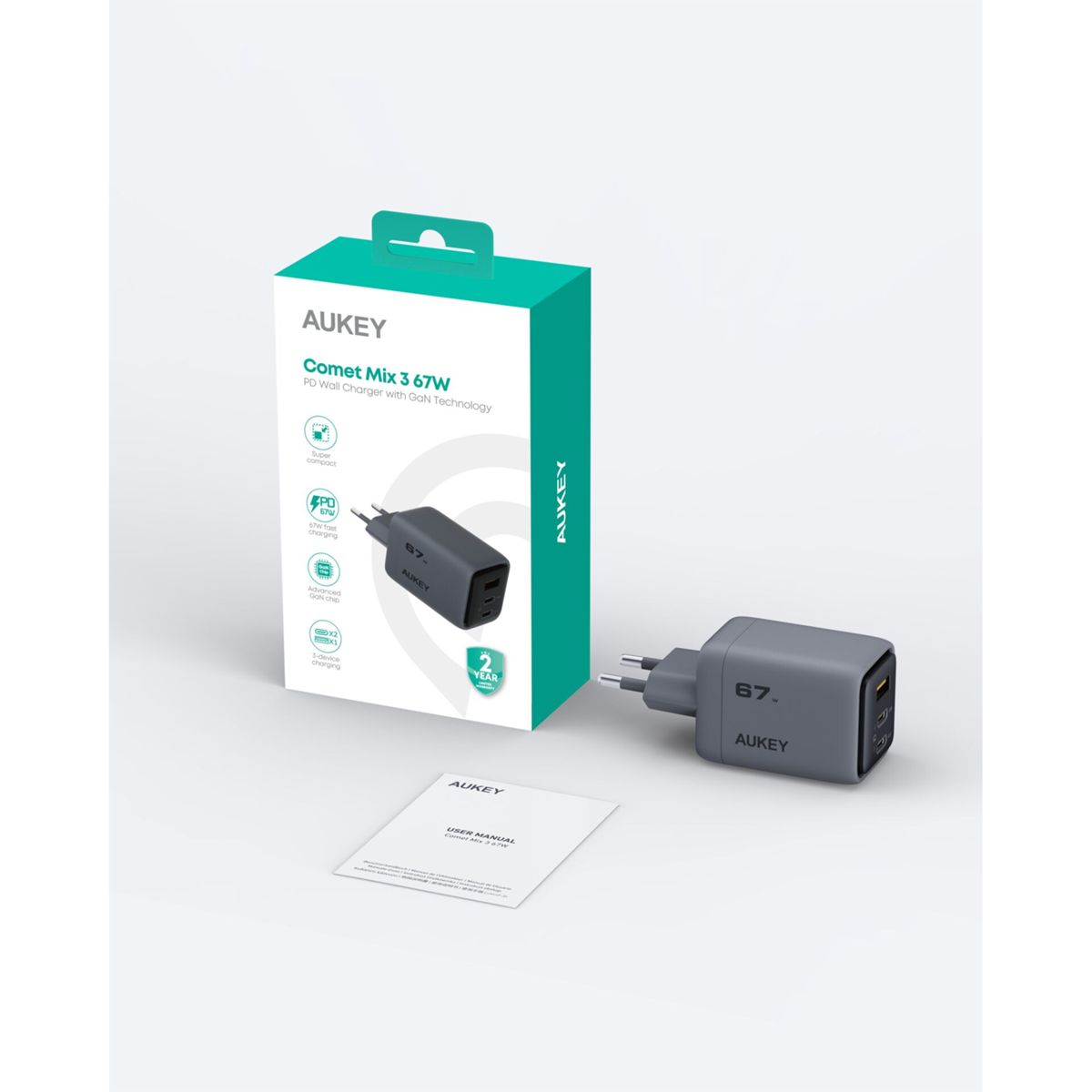 Un cargador AUKEY gris está junto a su caja, que es verde y blanca. Un manual de usuario se encuentra delante.