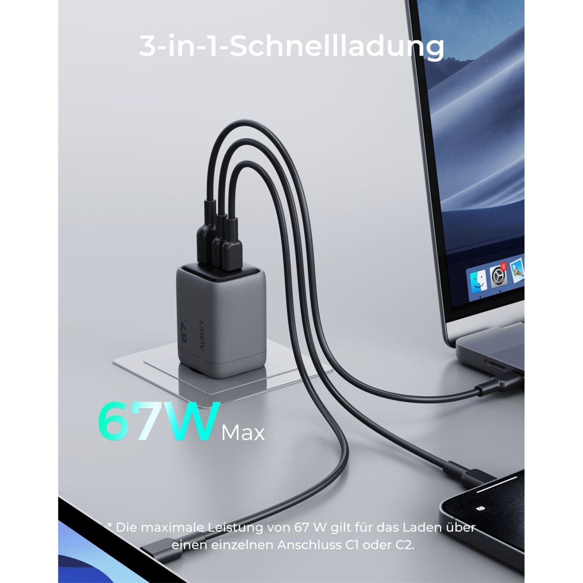Un cargador AUKEY gris con tres cables conectados a una laptop y un teléfono. El texto en el cargador dice 67W Max.