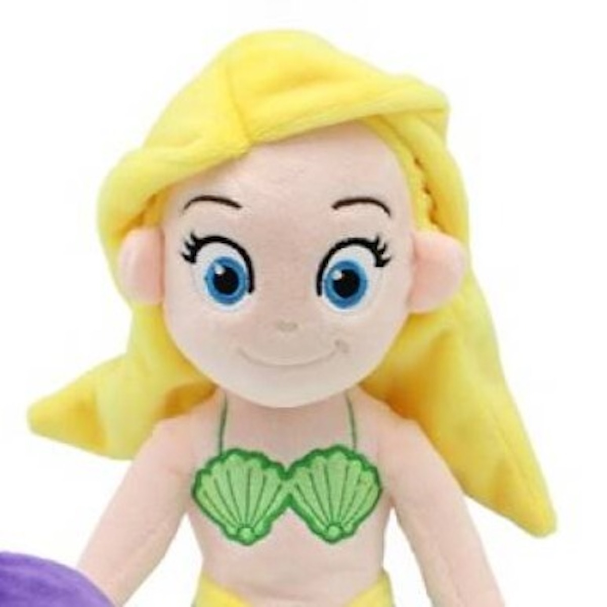 Eine Plüschpuppe einer Meerjungfrau mit gelbem Haar, blauen Augen, einem grünen Muscheloberteil und einem gelben Schwanz. Sie hat einen weißen Hintergrund.