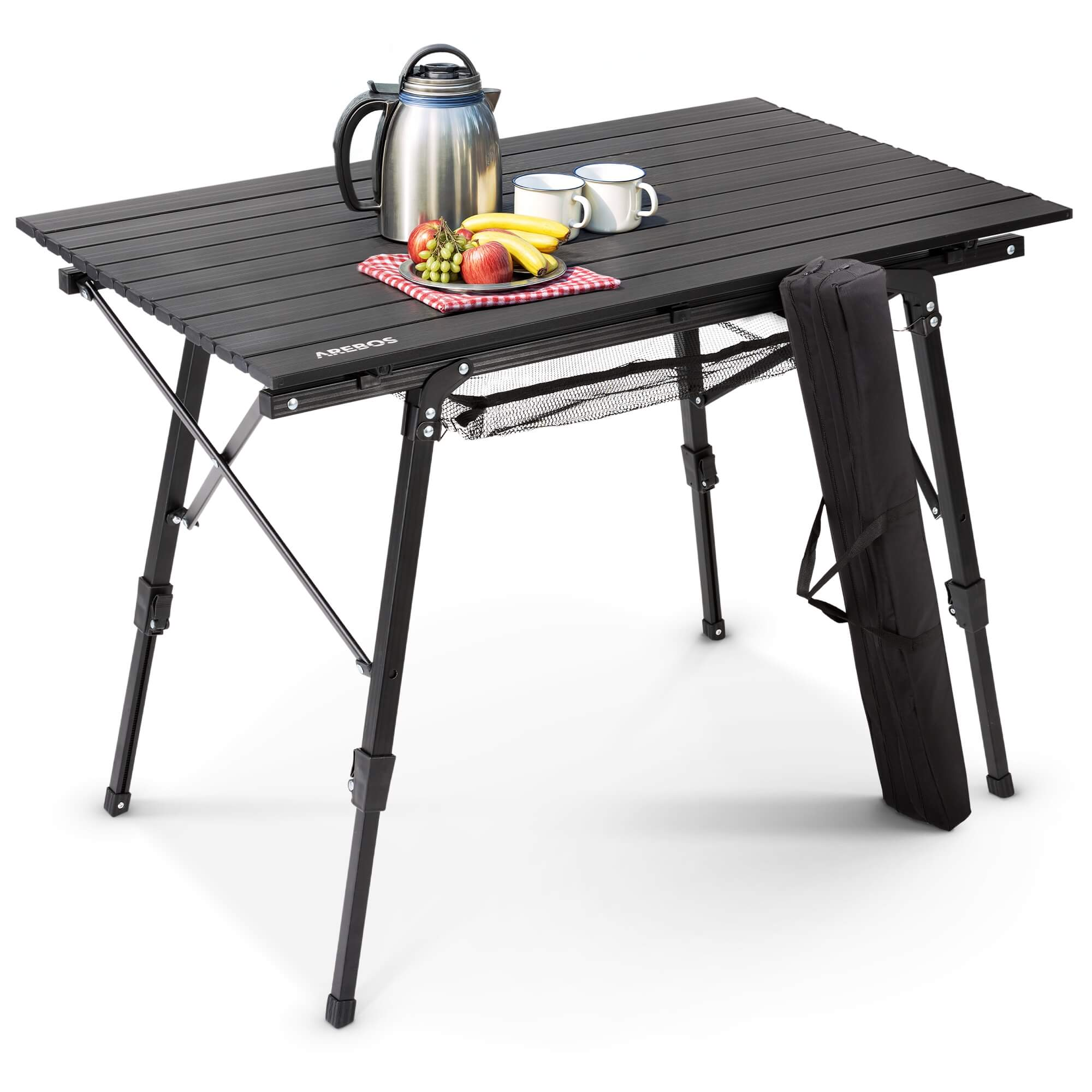 Ein schwarzer Klapptisch mit Obst, Tassen und einem Wasserkocher. Eine schwarze Tasche ist befestigt. Der Tisch steht vor weißem Hintergrund.