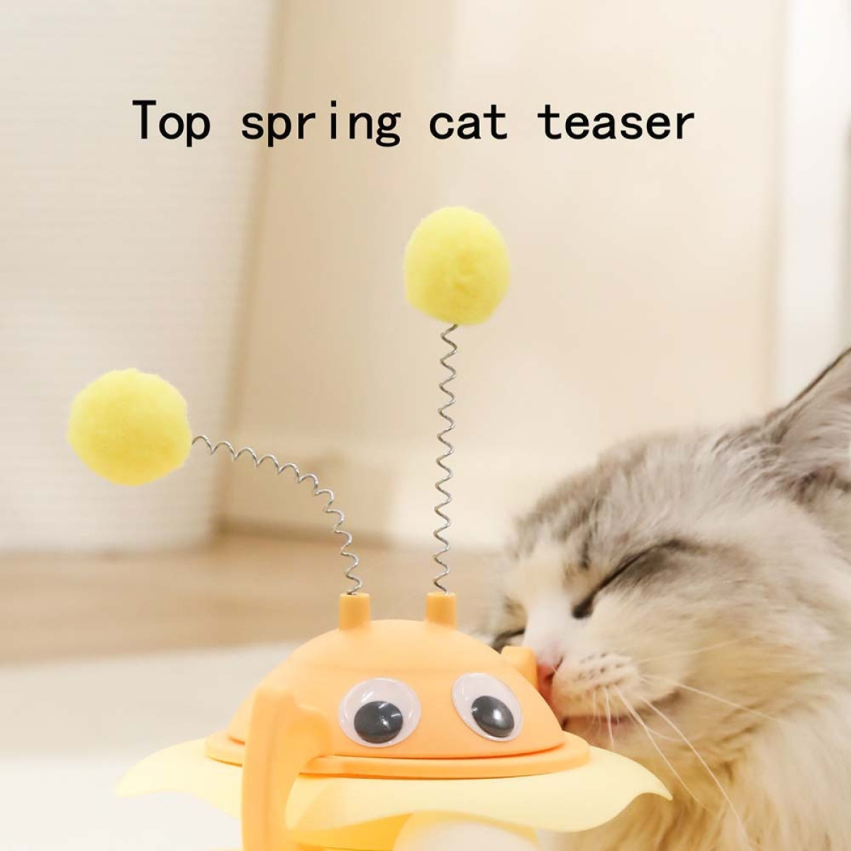 Ein Katzenspielzeug mit gelben Pompons und Federn. Eine Katze schmiegt sich an das Spielzeug. Das Spielzeug ist orange und gelb, mit dem Text 'Top spring cat teaser'.