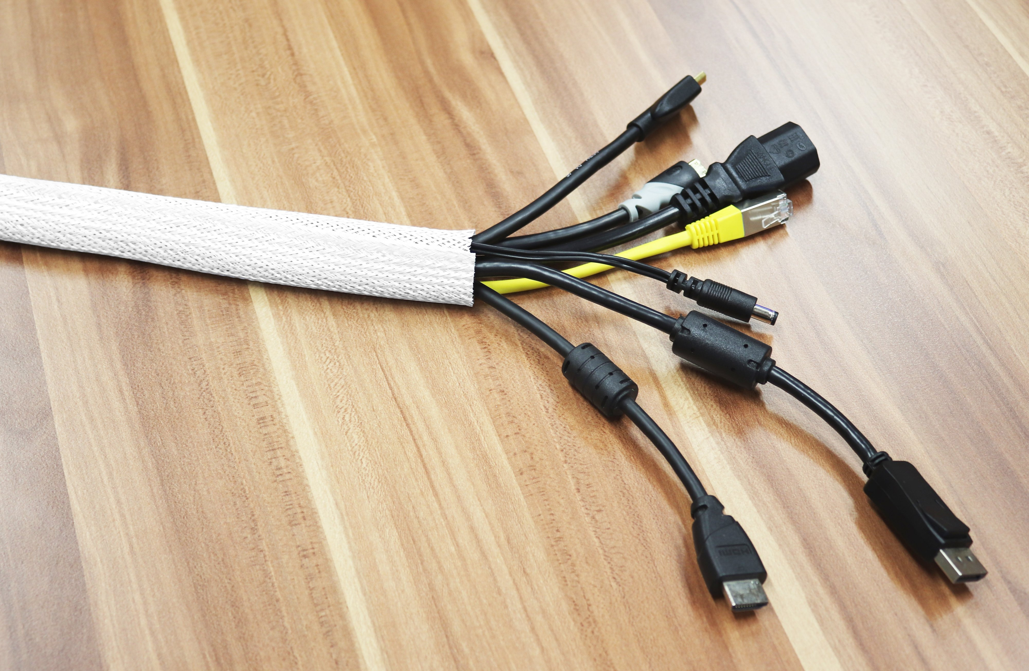 Mehrere schwarze Kabel kommen aus einer weißen Kabelhülse. Verschiedene Stecker an den Enden, auf Holzmaserung.