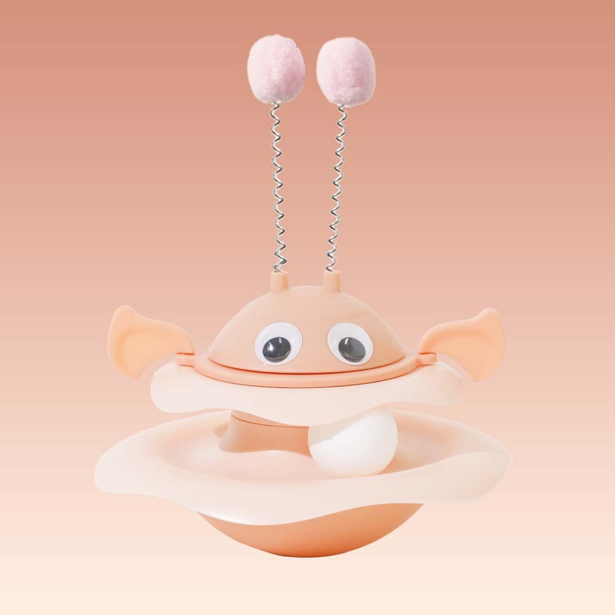 Un giocattolo per gatti a forma di granchio con due pompon rosa su molle e una pallina bianca in un piatto. Colori pesca e bianco.