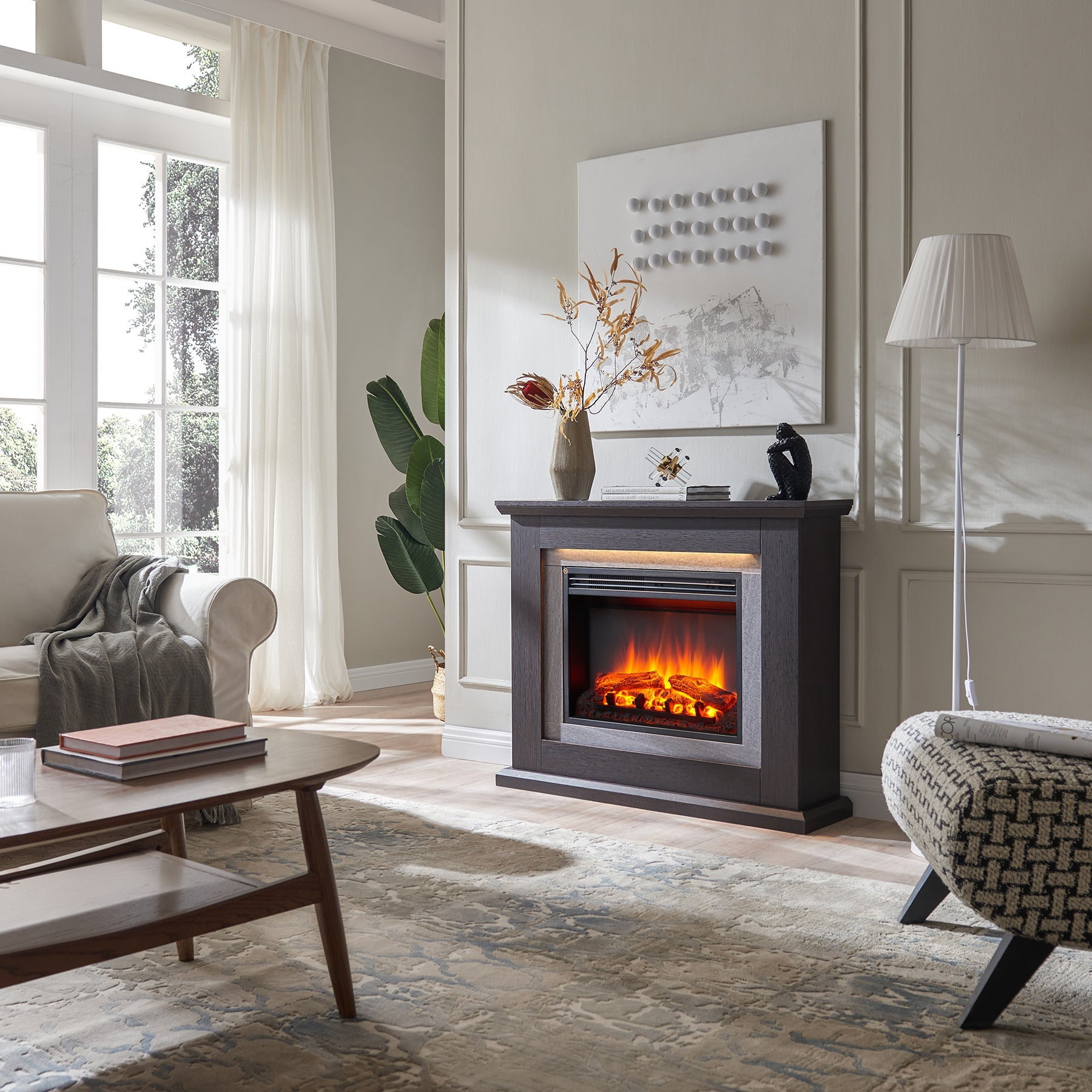 Ein Wohnzimmer mit Kamin. Ein Sofa, ein Couchtisch und ein gemustertes Ottoman sind im Raum. Ein großes Fenster befindet sich links.