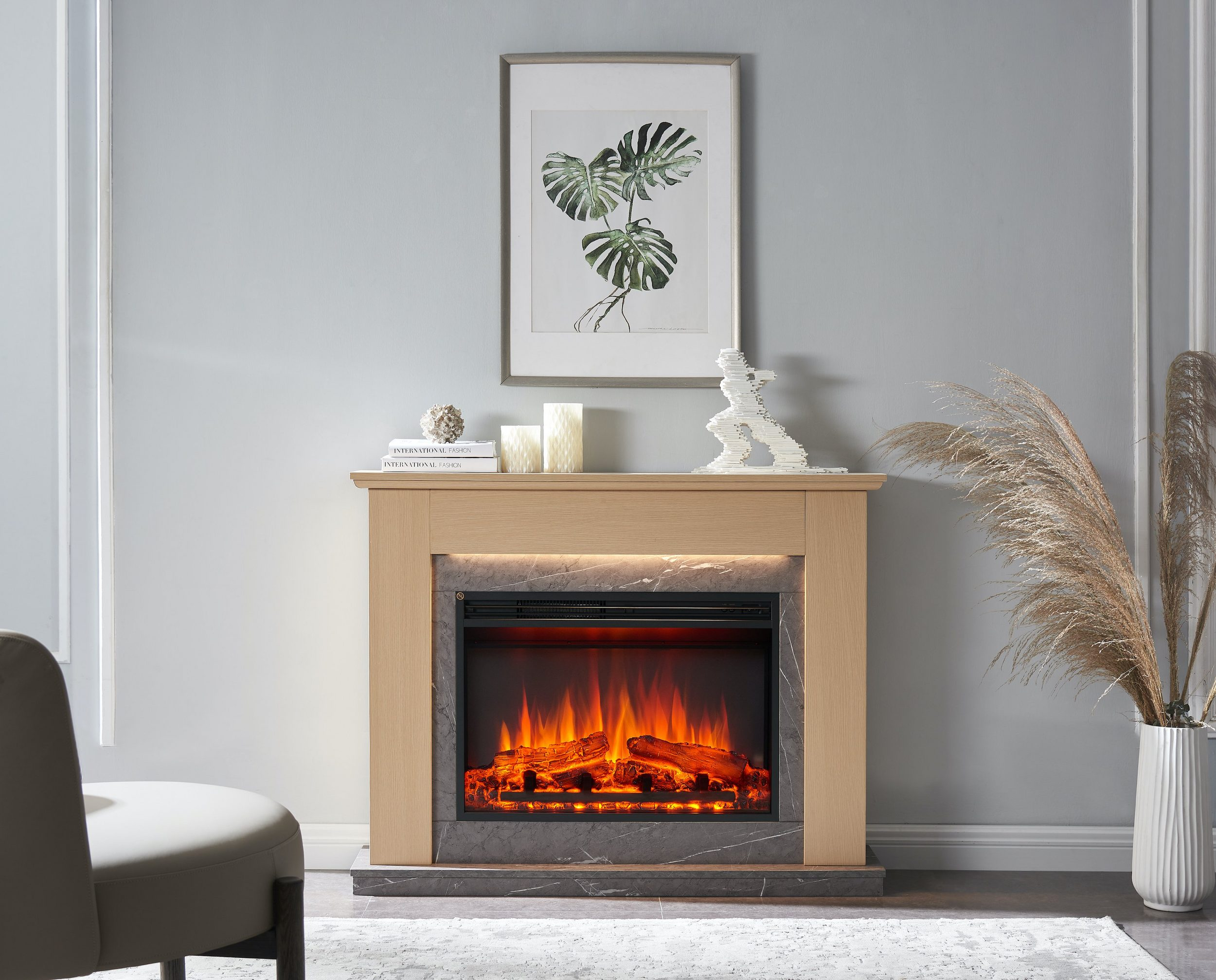 Kamin mit Flammen, gerahmter Pflanzenkunst, Kerzen und Dekor. Mit einer weißen Vase mit hohen, getrockneten Pflanzen.