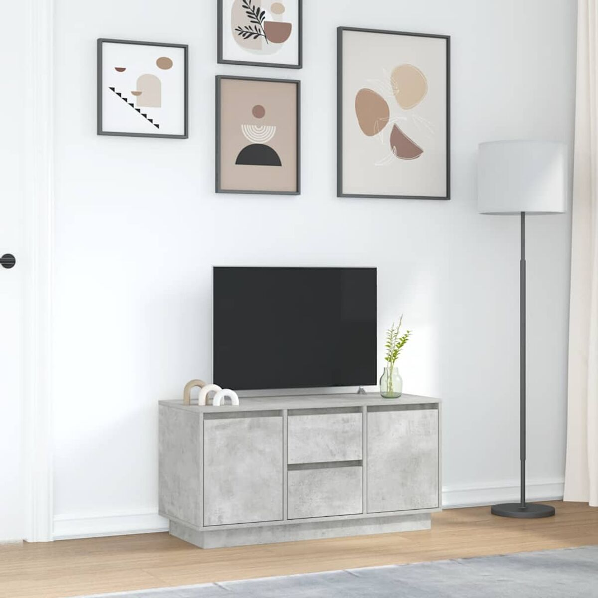 Ein Wohnzimmer mit Fernseher auf einem grauen Schrank. Kunst an der Wand, eine Lampe und eine Blumenvase.