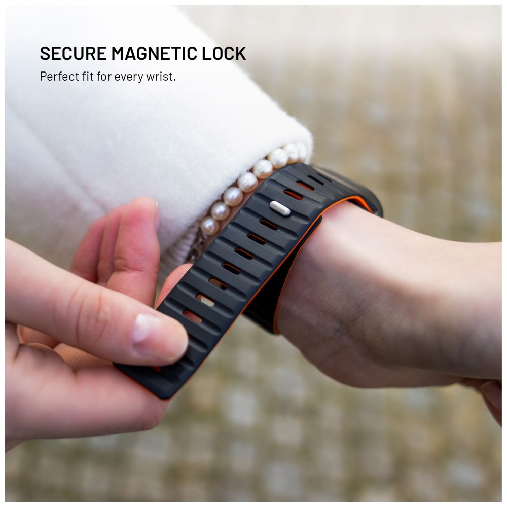 Eine Person befestigt eine schwarz-orange Smartwatch an ihrem Handgelenk. Das Uhrenarmband hat einen Magnetverschluss. Im Hintergrund ist ein weißer Mantel zu sehen.