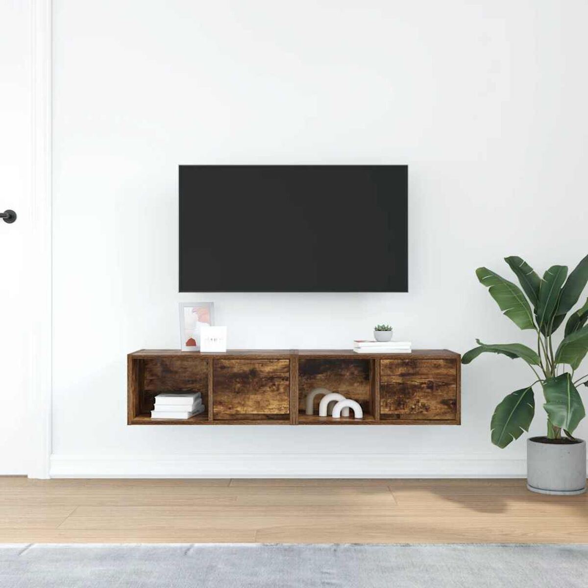 Ein Fernseher an einer weißen Wand über einem Holzregal. Rechts ist eine große Pflanze. Der Boden ist aus Holz.