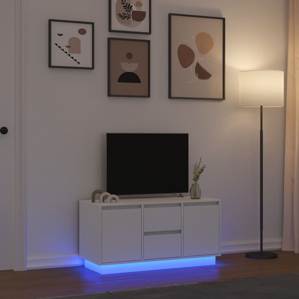 Ein Wohnzimmer mit Fernseher auf einem weißen Schrank. Wandkunst über dem Fernseher. Eine Stehlampe und blaue LED-Leuchten unter dem Schrank.
