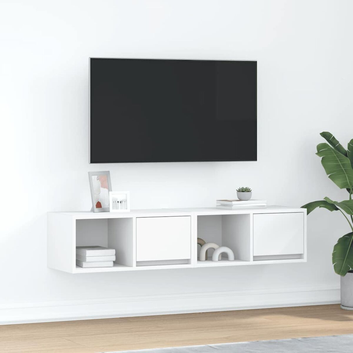 Eine wandmontierte weiße TV-Konsole mit einem schwarzen Fernseher darüber. Dekorative Gegenstände und eine Pflanze rechts.