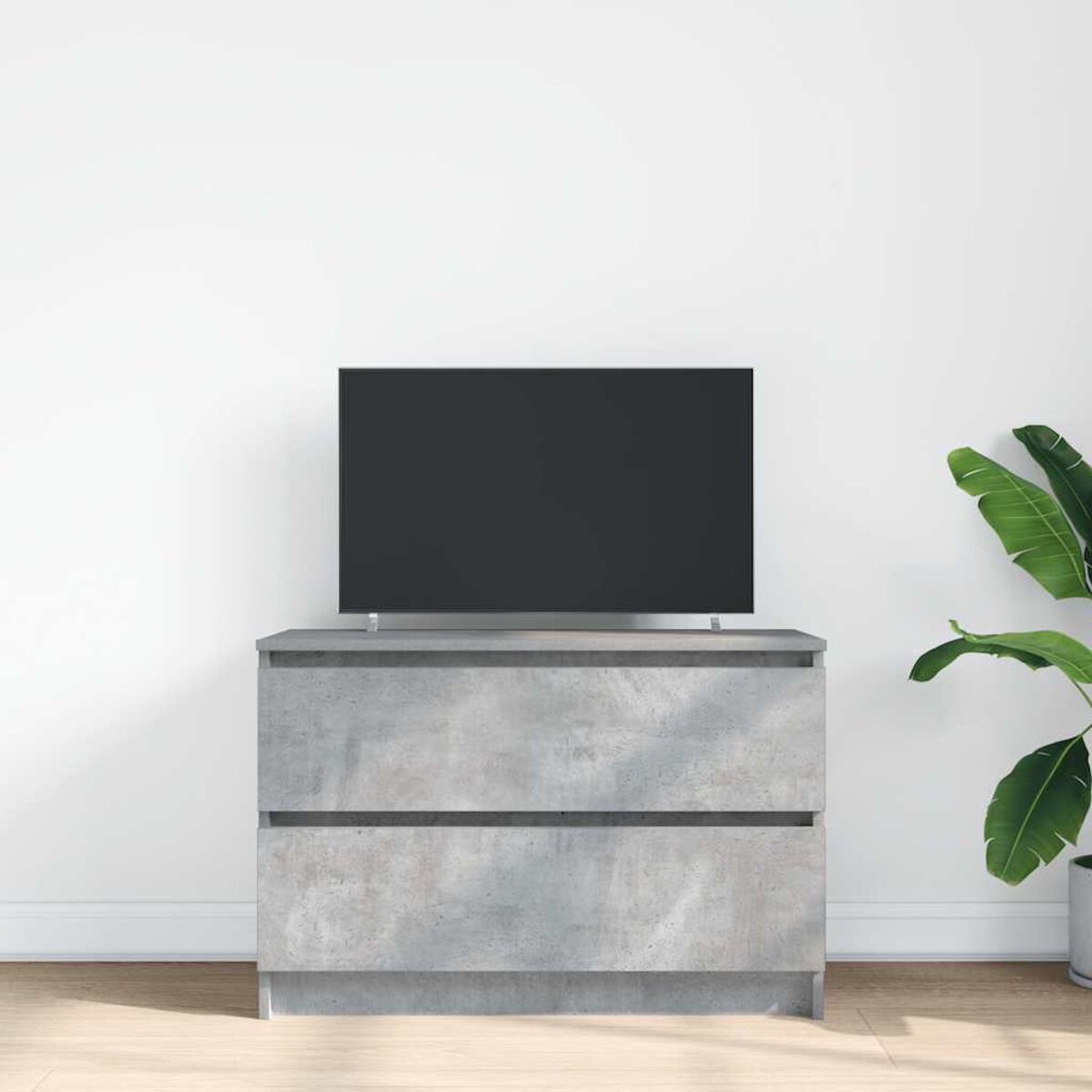 Graue Kommode mit schwarzem Fernseher. Rechts steht eine Topfpflanze. Die Wand ist weiß.