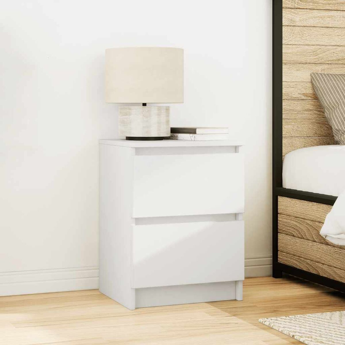Weißer Nachttisch mit Lampe und Büchern. Holz-Bettrahmen im Hintergrund. Helle beige Wand und Boden.