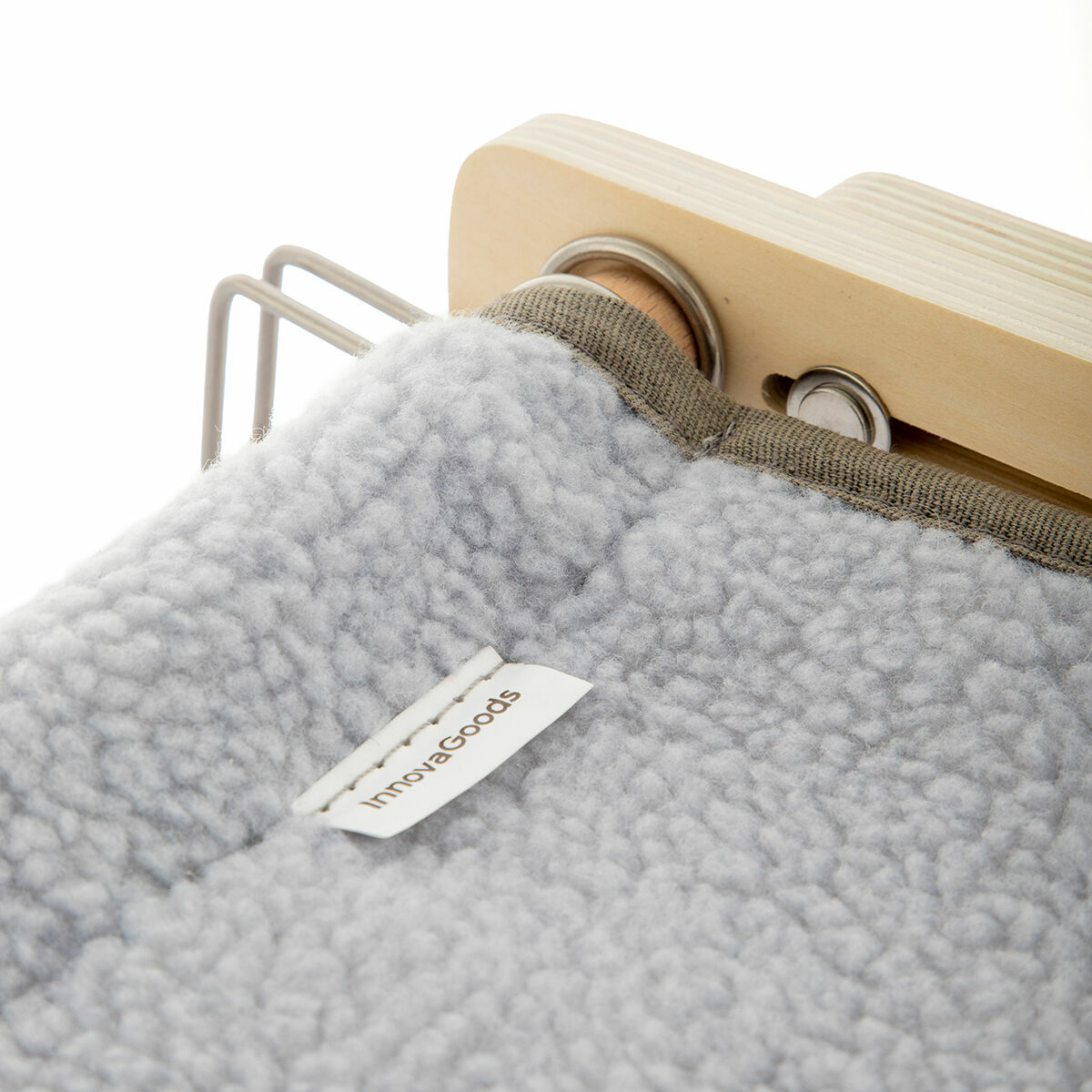 Un primo piano mostra un tessuto grigio chiaro e soffice con un'etichetta InnovaGoods, attaccato a un telaio di legno. Sono visibili anche barre di metallo.