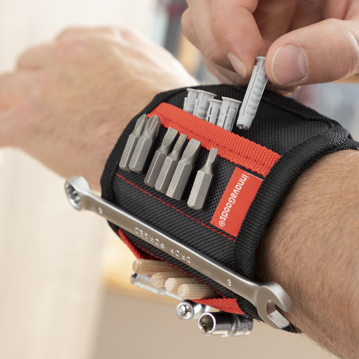 Il polso di una persona tiene un organizer per attrezzi con punte, tasselli e una chiave. La mano inserisce un tassello. Logo InnovaGoods.