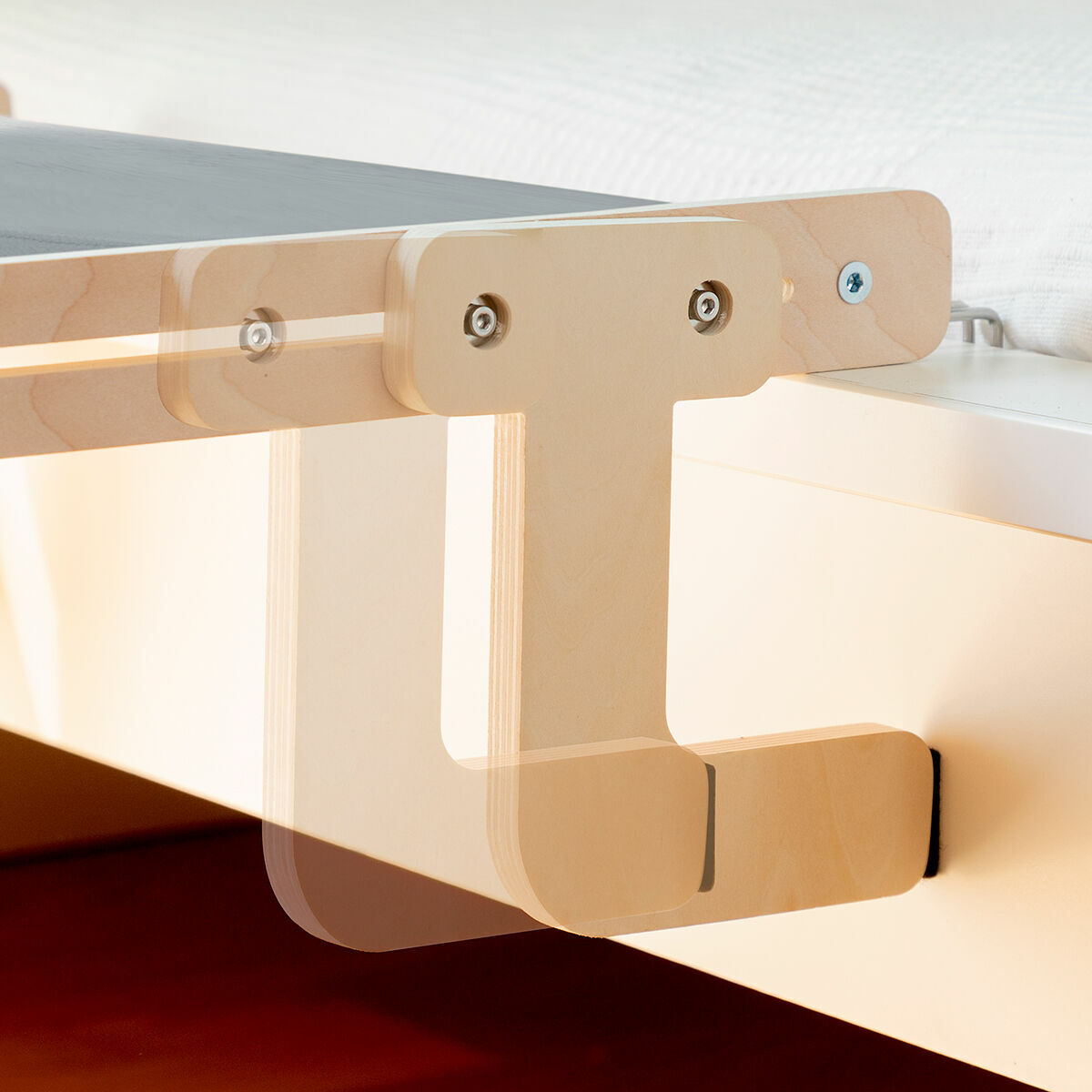 Supporto per struttura letto in legno. Legno chiaro con viti metalliche. Fissato a un muro bianco e una superficie marrone scuro.