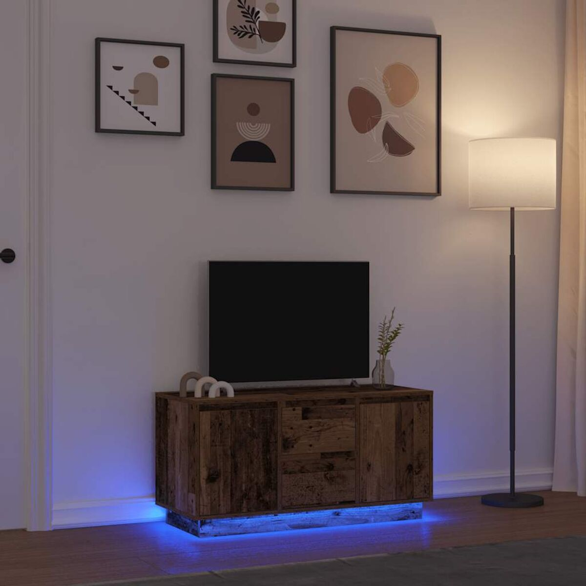 Ein Fernseher auf einem Holzschrank mit blauem Unterlicht, gerahmte Kunst an der Wand und eine Stehlampe.