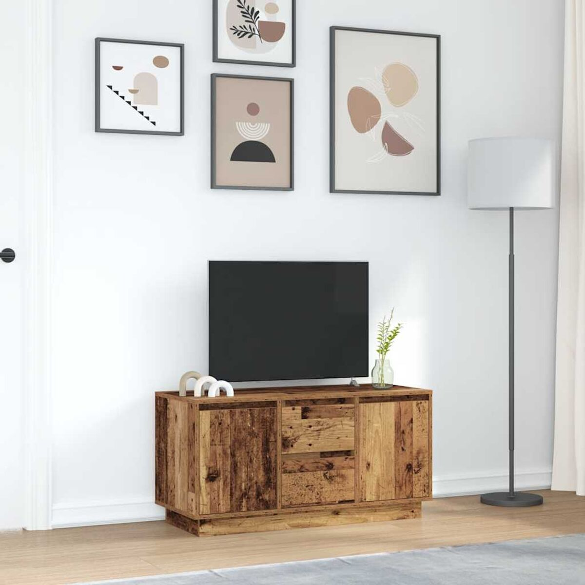 Ein Holzschrank mit einem Fernseher. Vier gerahmte Kunstwerke hängen darüber. Rechts steht eine Lampe, mit einer weißen Wand.
