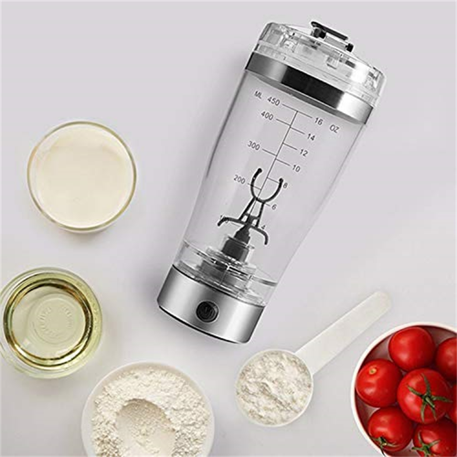 Ein durchsichtiger Mixer mit Maßen, umgeben von kleinen Schalen mit Zutaten wie Milch, Öl, Pulver und Tomaten.