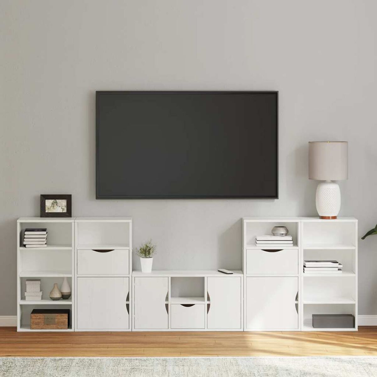 Moderne Wohnzimmereinrichtung mit großem Fernseher, weißen Schränken, Lampe und Dekoelementen. Holzfußboden und graue Wand.