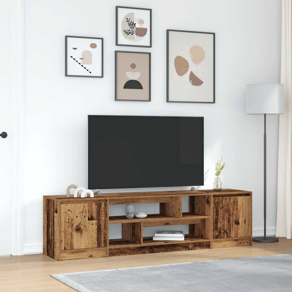 Wohnzimmer mit Fernseher auf einem Holzschrank, gerahmter Kunst an der Wand, Stehlampe und einem Teppich. Neutrale Farben dominieren.