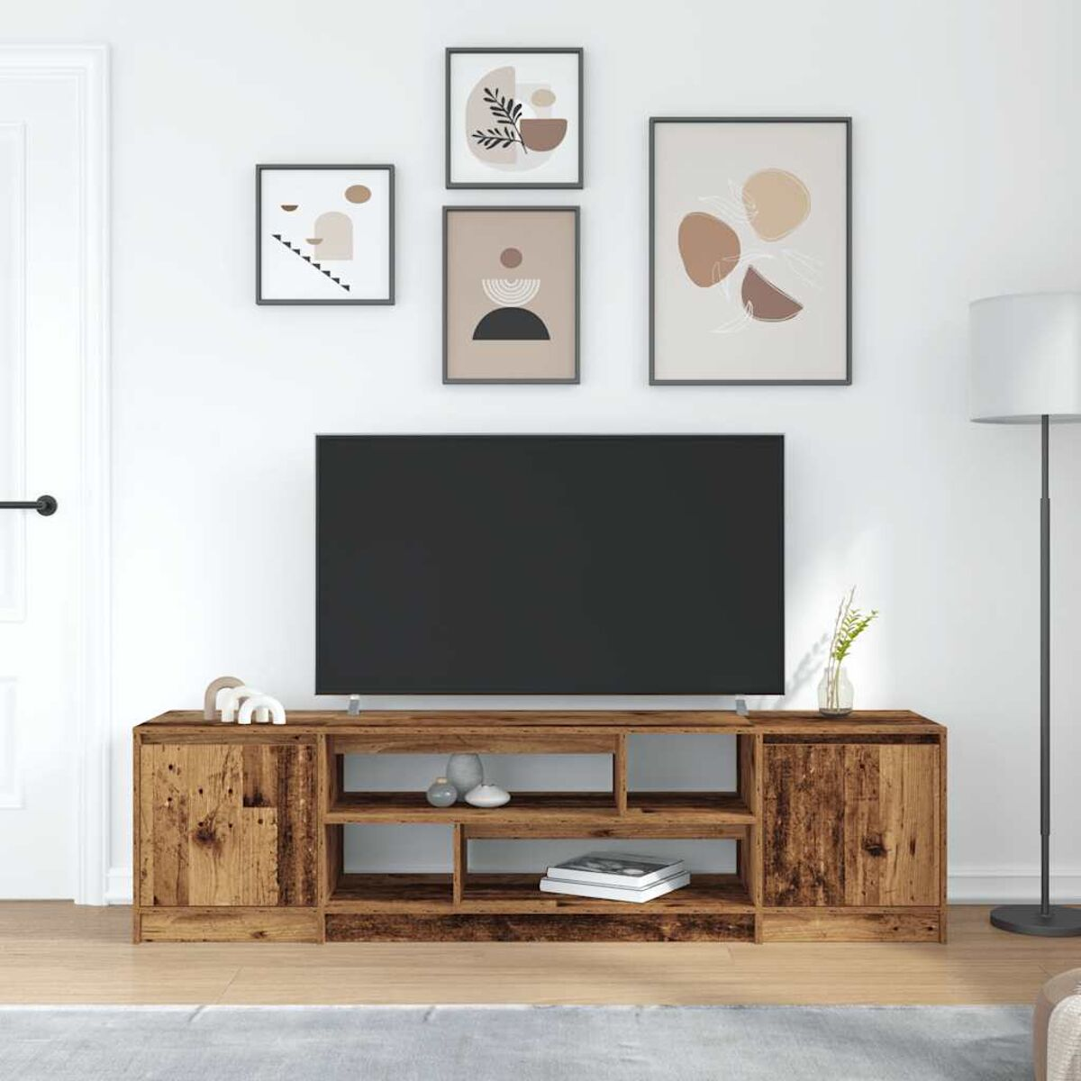 Wohnzimmer mit Fernseher auf einem Holzständer, gerahmte Kunst an der Wand. Rechts steht eine Lampe. Der Boden ist hellbraun.
