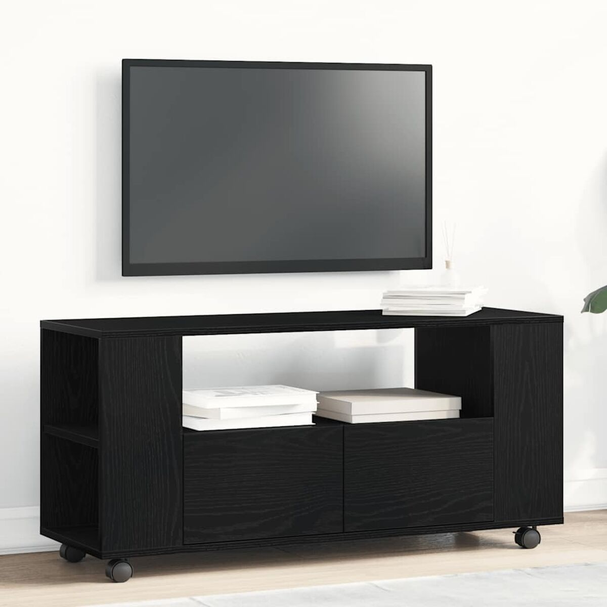 Ein schwarzer TV-Ständer mit einem Fernseher an der Wand darüber. Auf dem Ständer liegen Bücher.