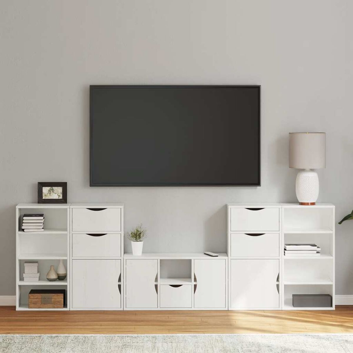 Eine weiße Unterhaltungseinheit mit großem Fernseher, Schränken, Schubladen, Regalen und einer Lampe. Eine kleine Pflanze und ein Bilderrahmen sind vorhanden.