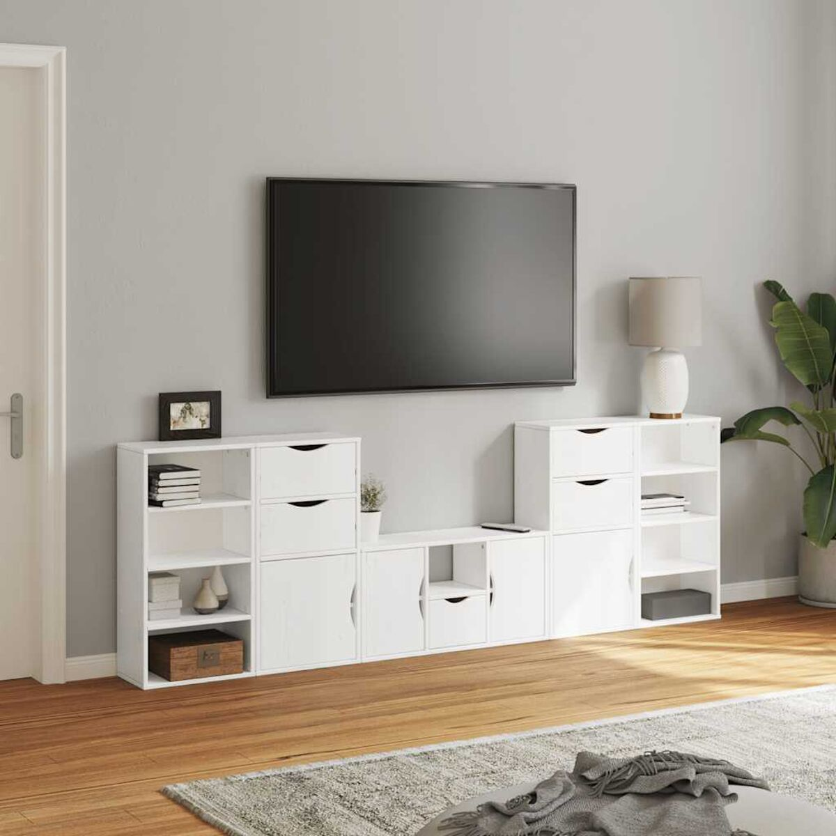 Ein weißes Entertainmentcenter mit Fernseher, Schubladen, Regalen und Dekor. Eine Lampe und eine Pflanze sind in der Nähe. Holzboden und ein Teppich.