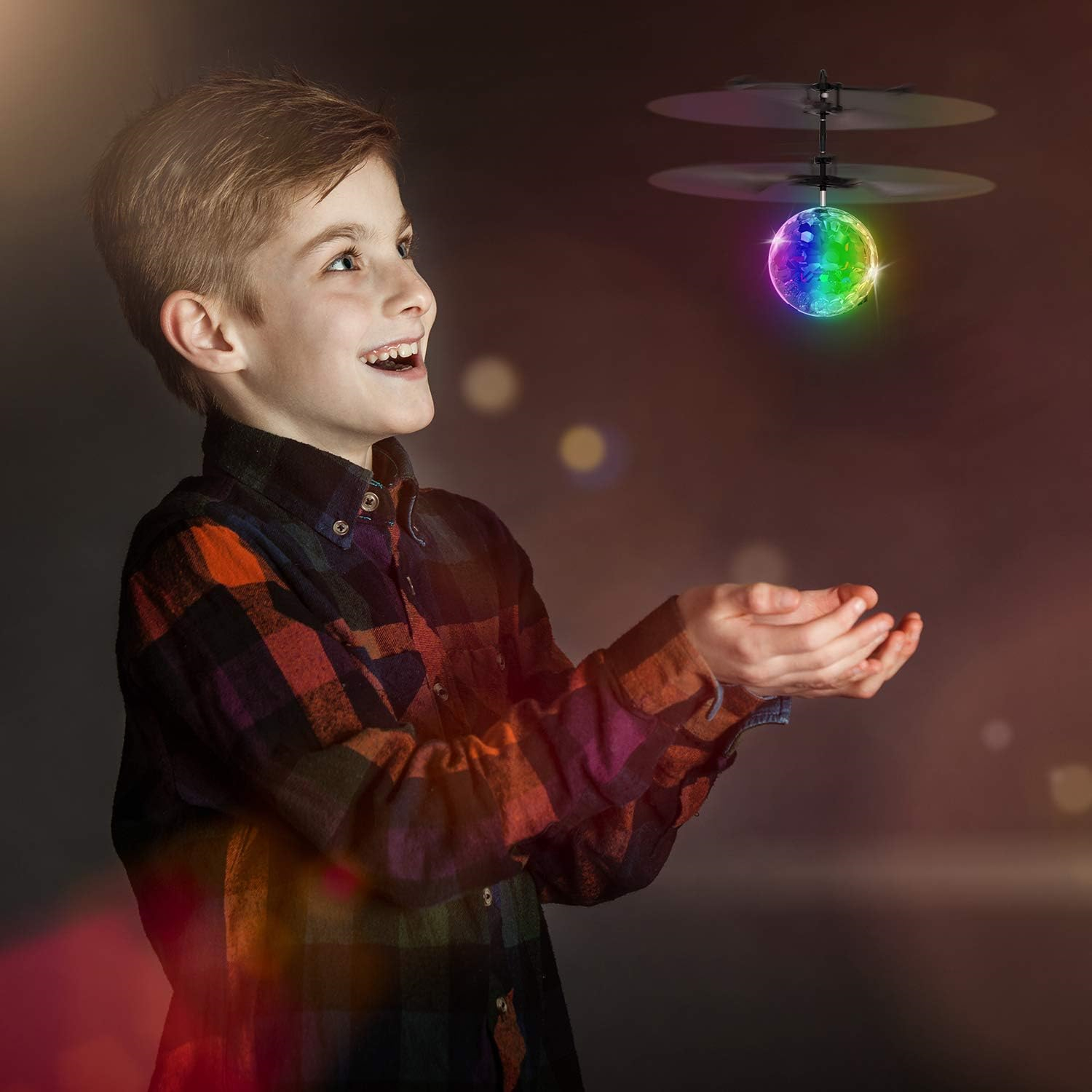 Ein Junge blickt auf eine bunte, leuchtende Kugel mit Propellern. Er lächelt und trägt ein kariertes Hemd mit ausgestreckten Händen.