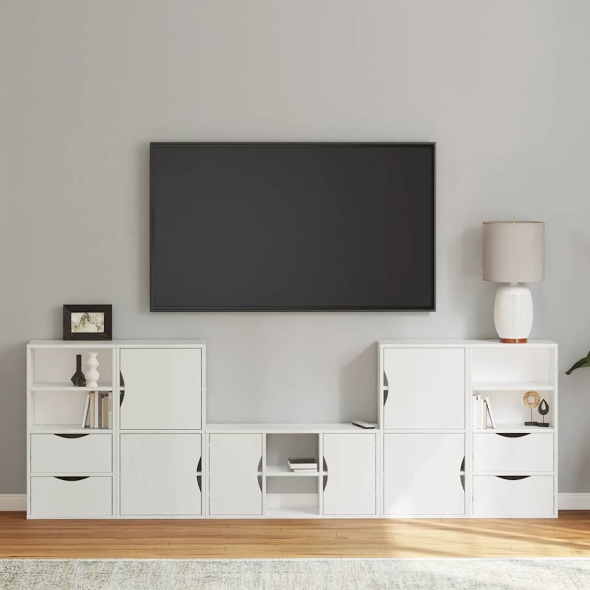 Ein Wohnzimmer mit einem Fernseher über einem weißen Schrank. Der Schrank hat Schubladen und Regale. Eine Lampe und Dekorationen sind sichtbar.