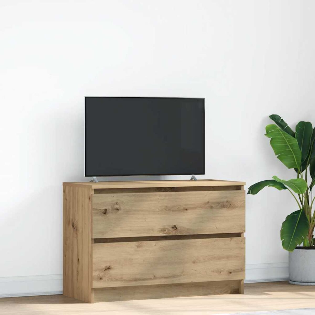 Ein Fernseher steht auf einer Holzkommode mit zwei Schubladen. Eine große Topfpflanze steht rechts an der weißen Wand.