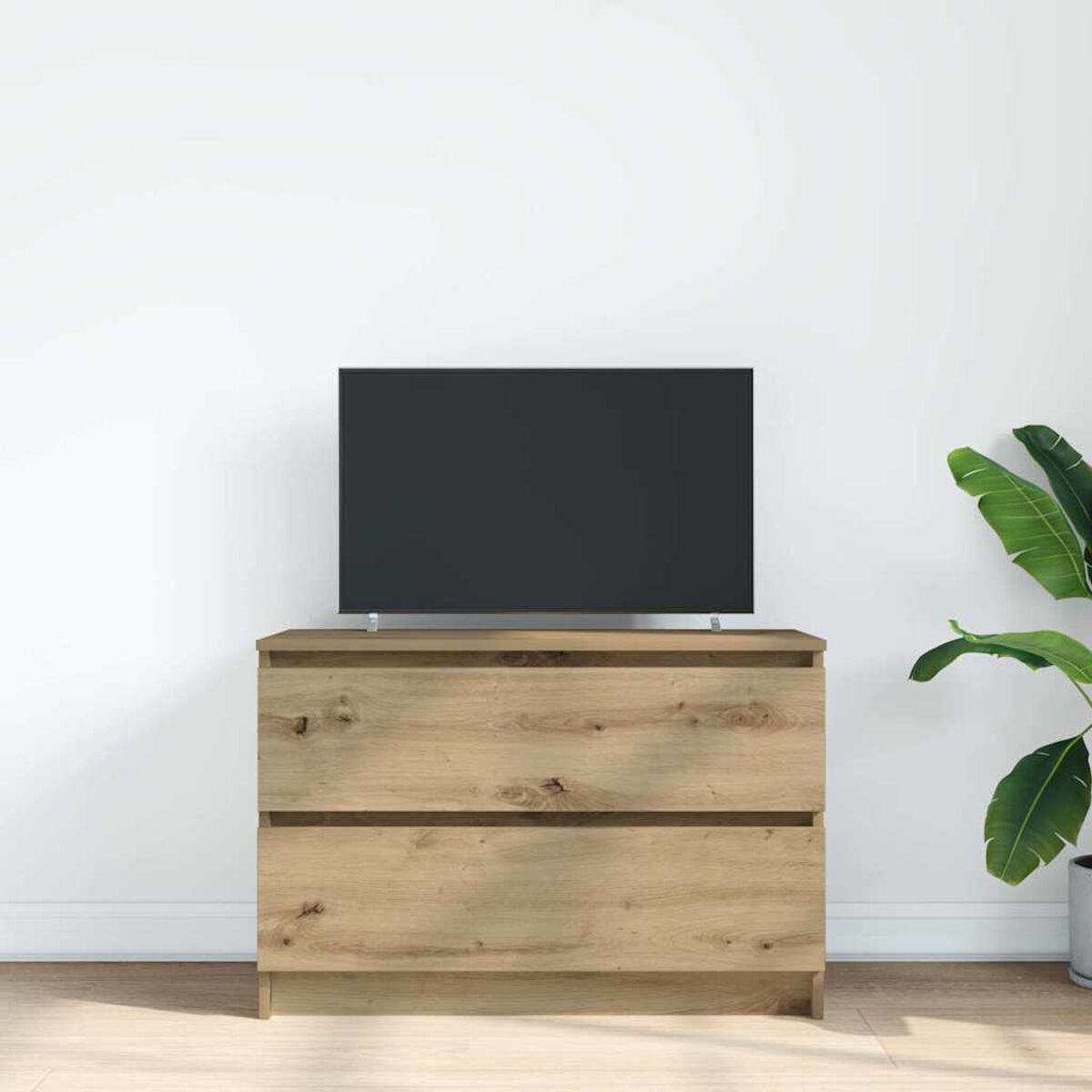 Eine Holzkommode mit zwei Schubladen trägt einen schwarzen Fernseher. Rechts eine Topfpflanze, vor einer weißen Wand.