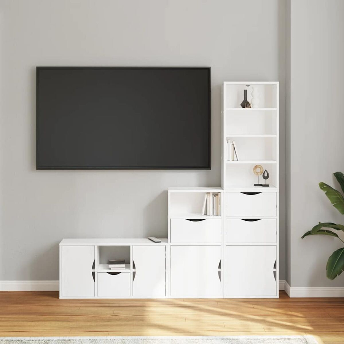 Ein an der Wand montierter schwarzer Fernseher über weißen Schränken und Regalen. Bücher und Dekorationen stehen auf den Regalen. Holzboden und eine Pflanze.