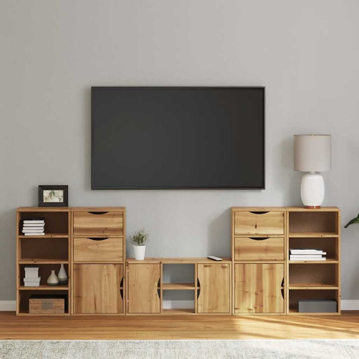Ein modernes Wohnzimmer. Ein großer Fernseher an einer grauen Wand. Darunter Holzschränke und Regale mit Dekor.