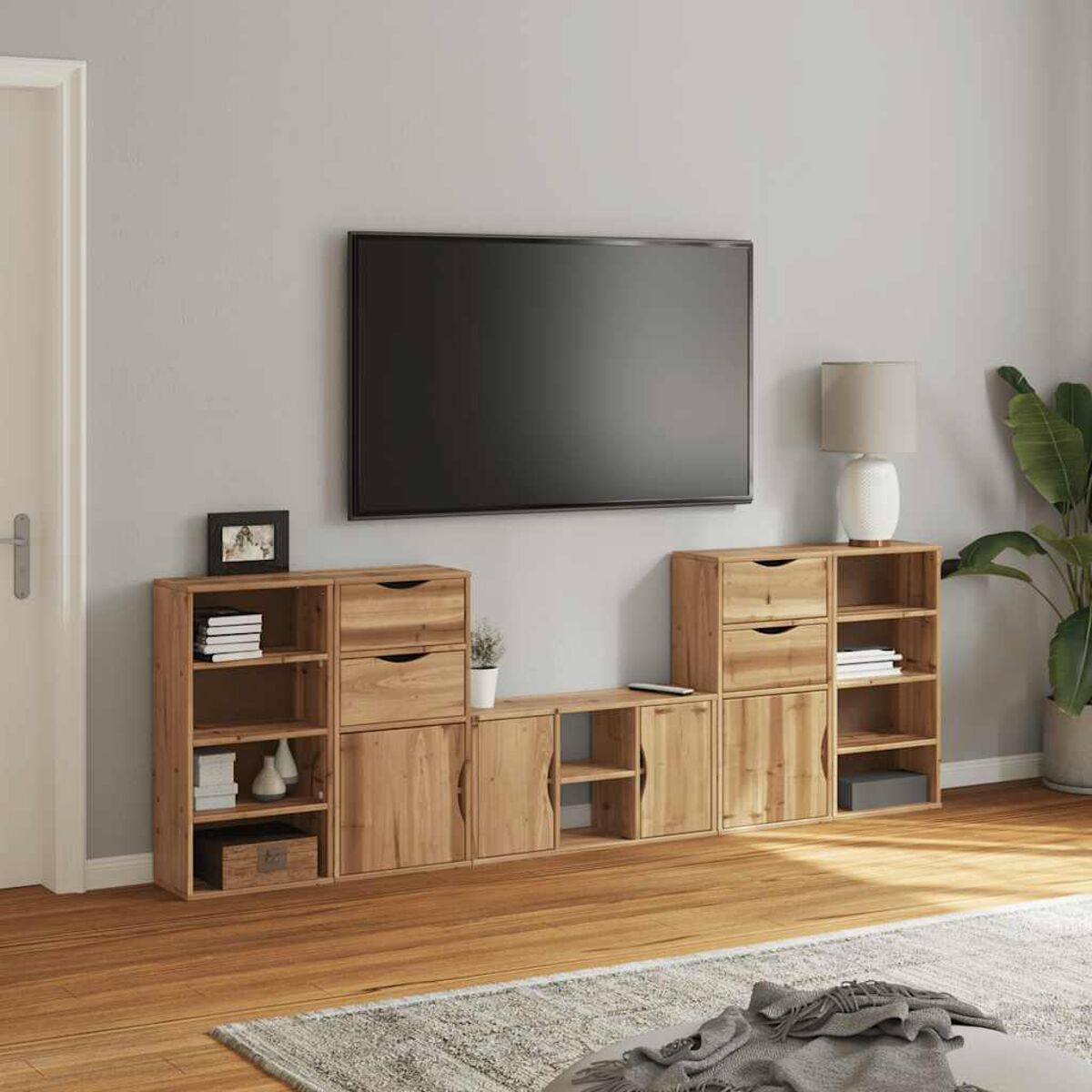 TV-Schrank aus Holz mit Schubladen, Regalen und einem großen schwarzen Fernseher an einer hellgrauen Wand.