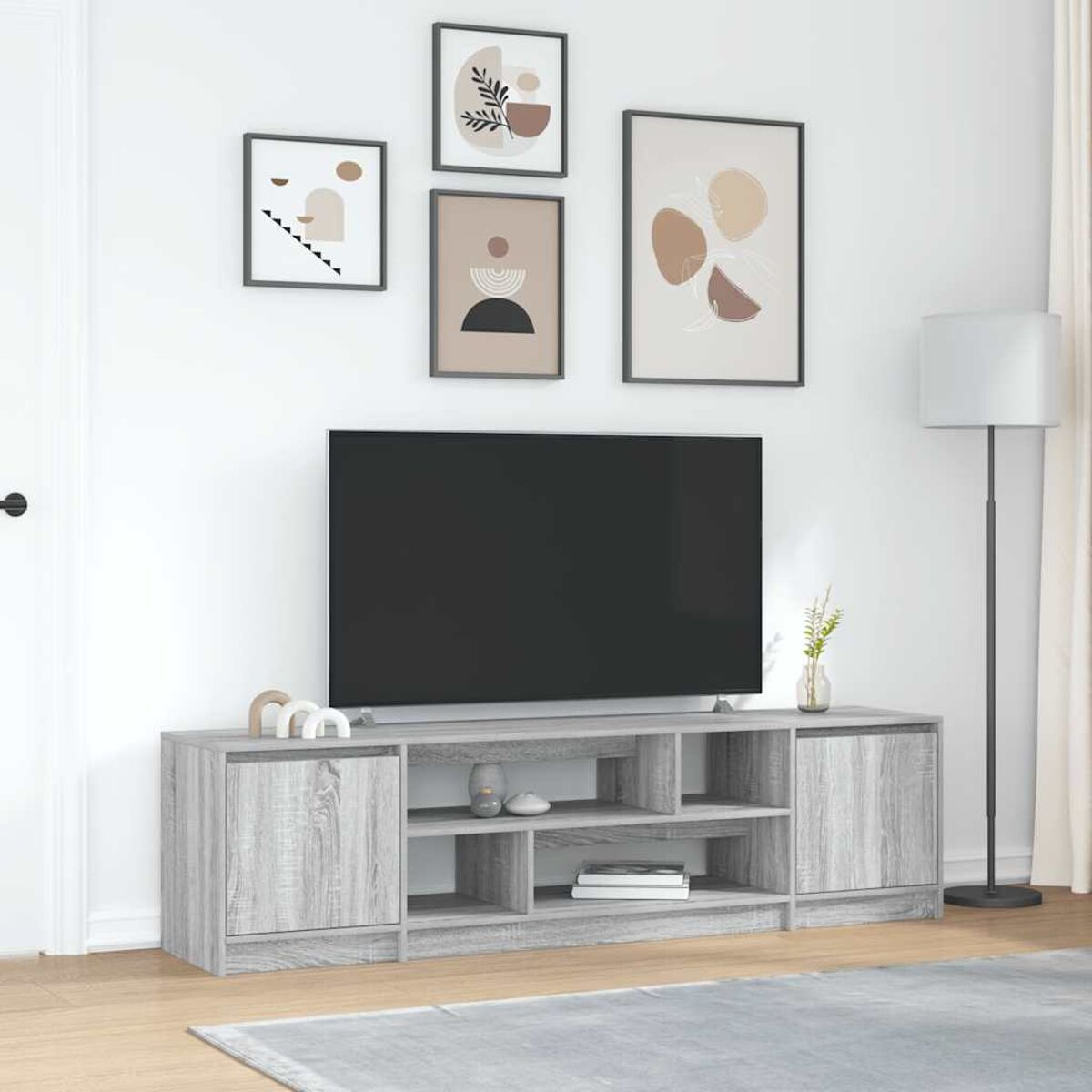Ein Wohnzimmer mit einem Fernseher auf einem grauen Schrank. Darüber gerahmte Kunst. Rechts steht eine Stehlampe. Ein grauer Teppich.