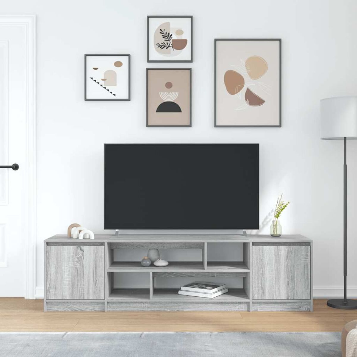 Grauer Fernsehständer mit schwarzem Fernseher. Kunstwerke hängen darüber. Rechts ist eine Lampe. Es gibt einen Teppich und Holzboden.