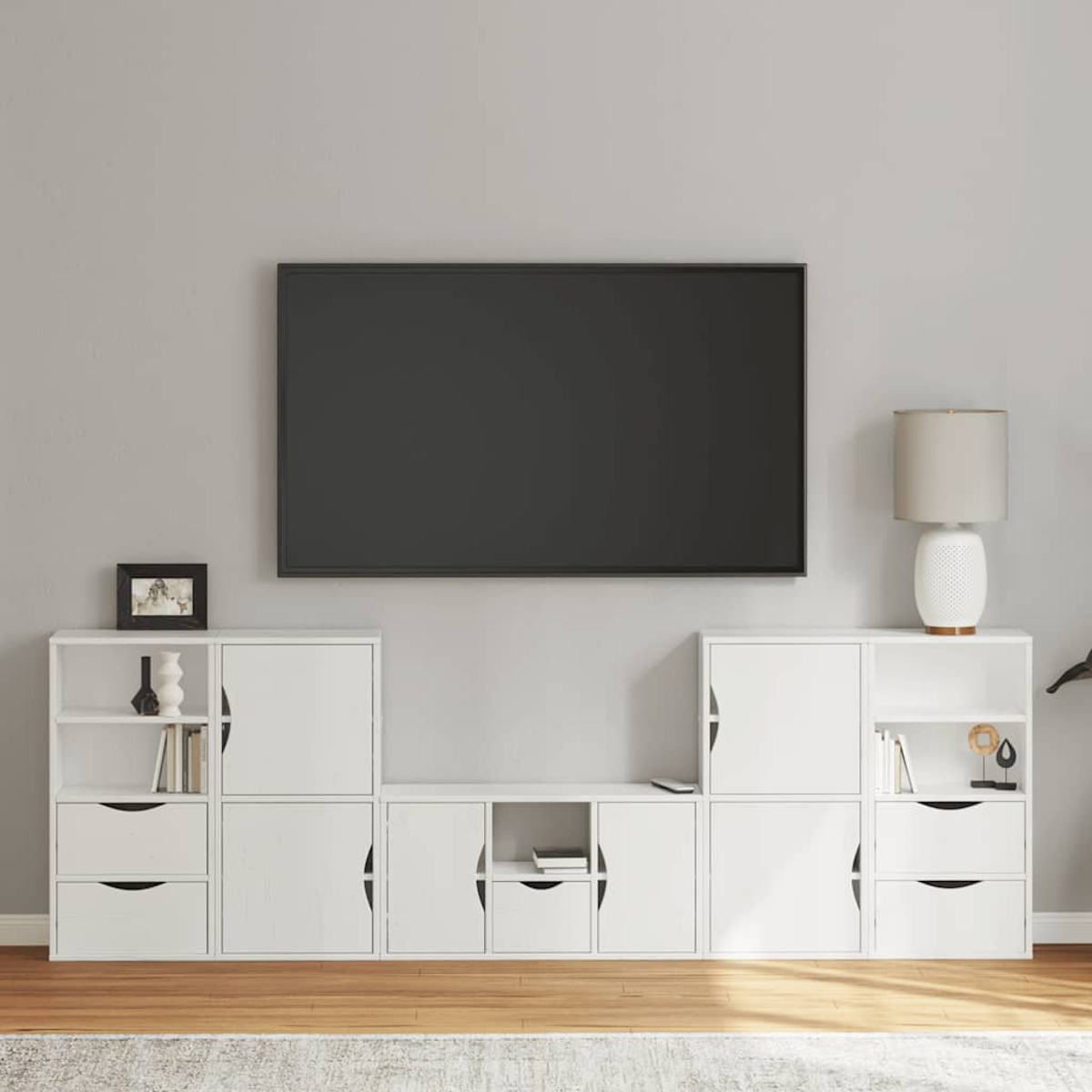Ein Wohnzimmer mit Fernseher, weißen Schränken, Lampe und Dekoration. Holzboden und graue Wand sind sichtbar.