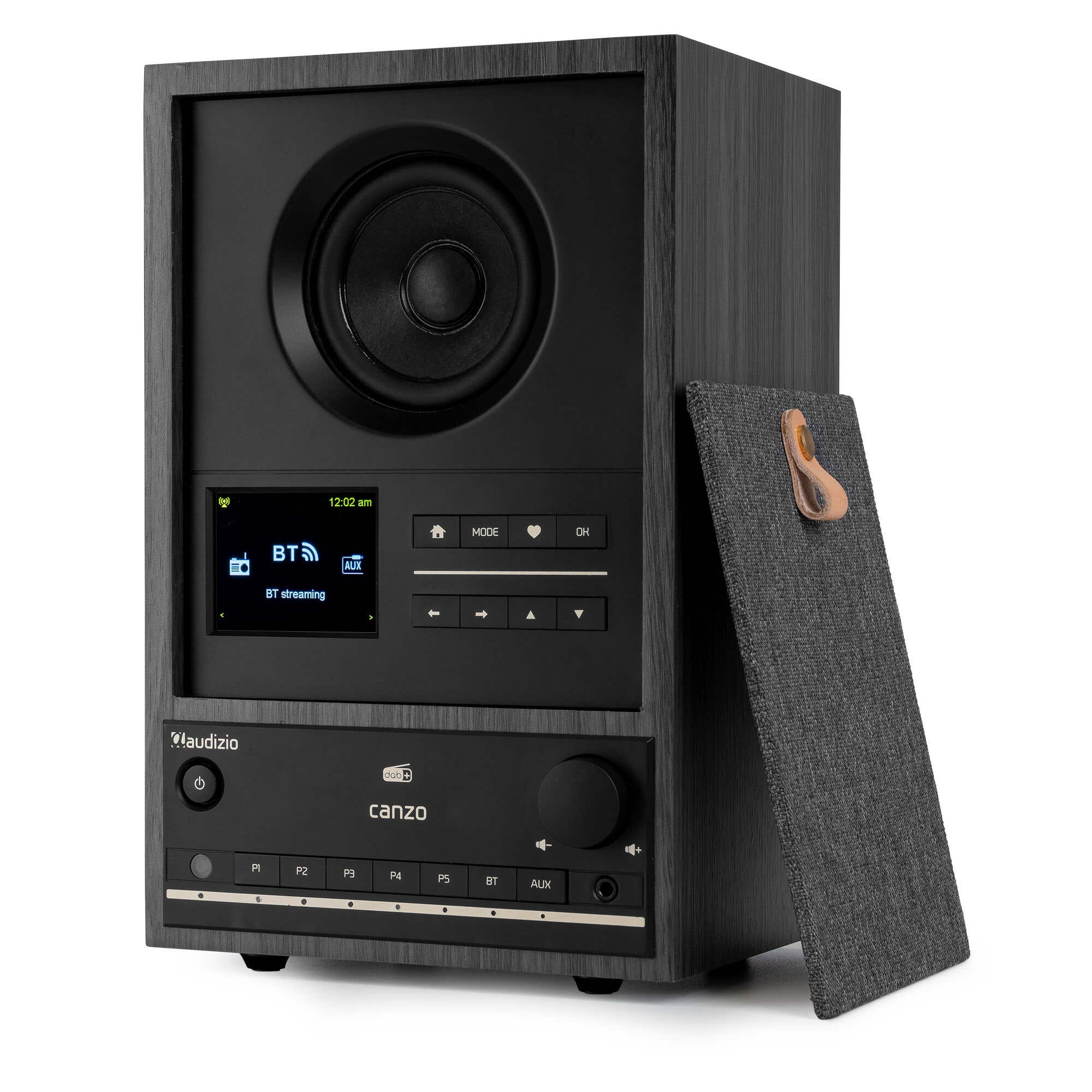 Altavoz negro con pantalla mostrando BT streaming. A la derecha, un soporte con lazo de cuero.