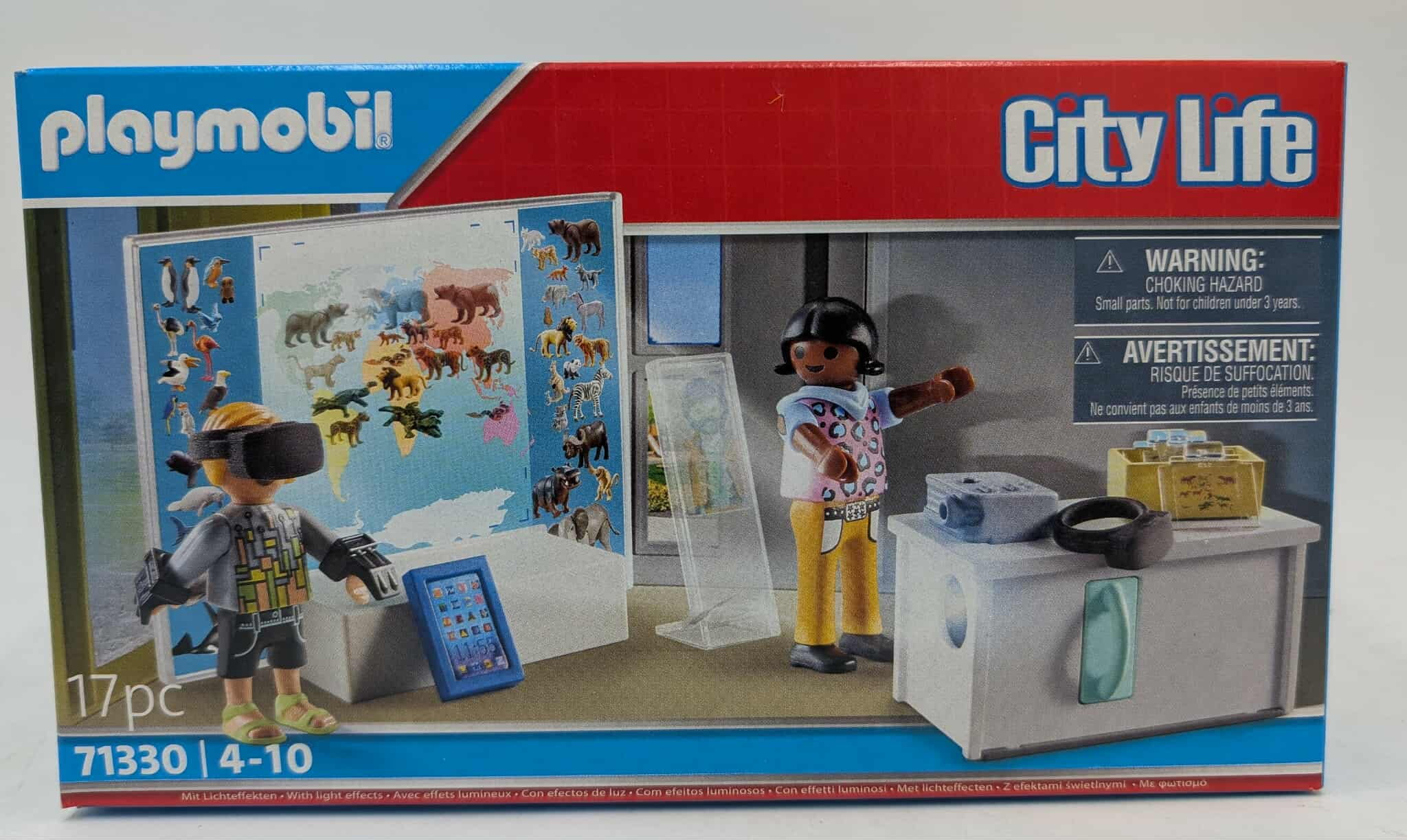 Zestaw Playmobil City Life. Zawiera figurki, mapę świata, zestaw VR, tablet i stół wystawowy. Obecne są etykiety ostrzegawcze.