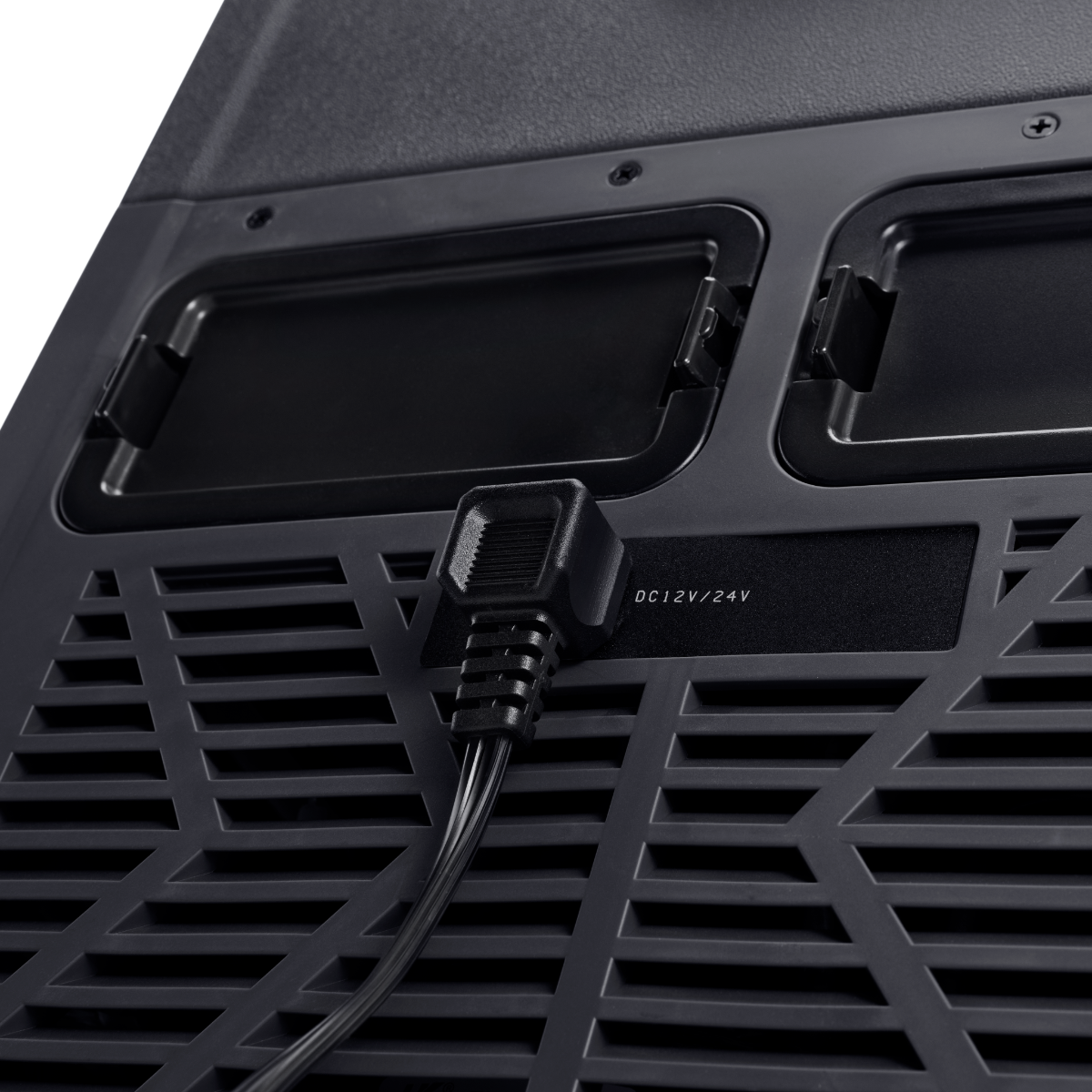 Primo piano del retro di un dispositivo nero. Presenta un cavo di alimentazione collegato. Sono visibili prese d'aria e pannelli. Il testo recita 'DC 12V/24V'.