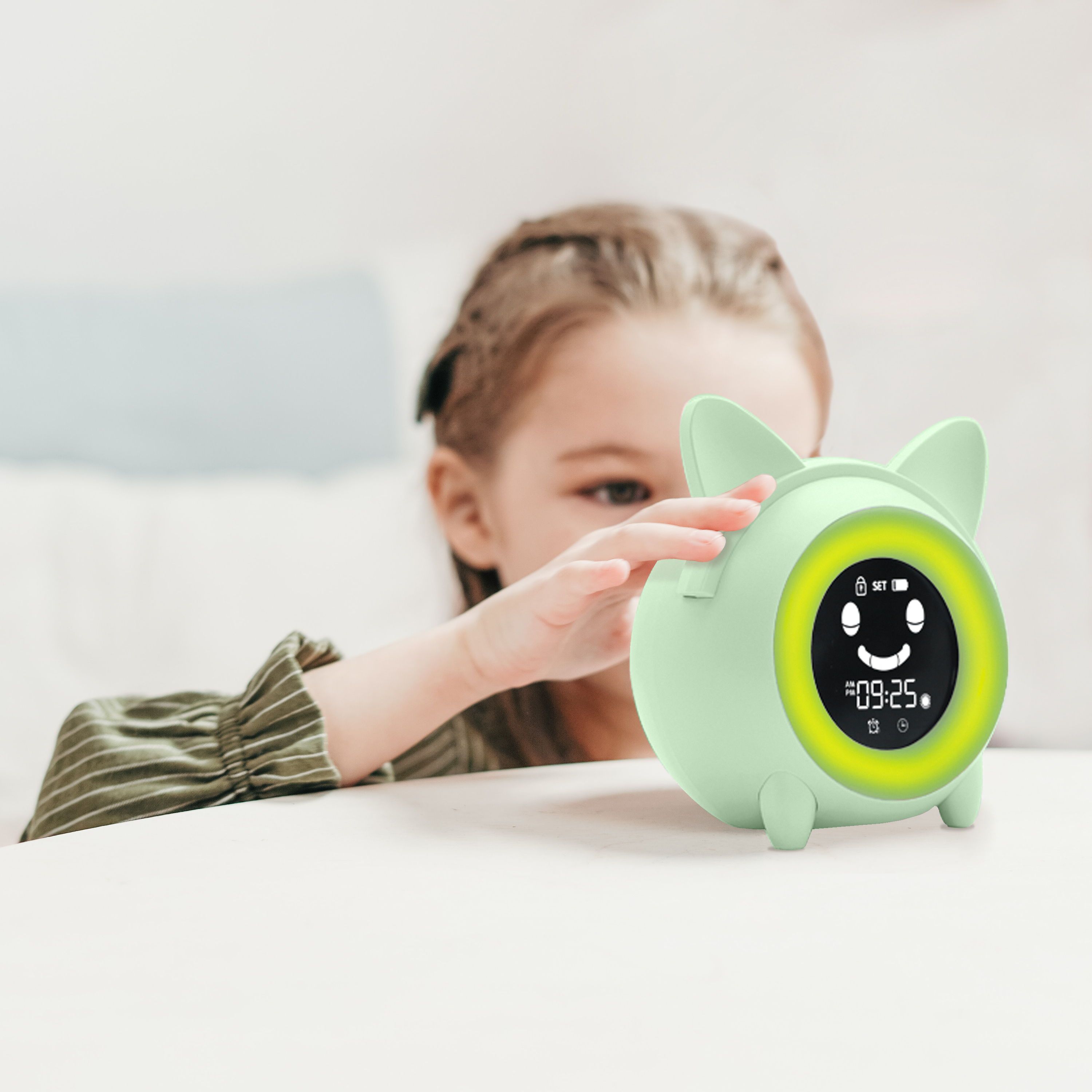 Un niño toca un despertador verde menta con diseño de orejas de gato. El reloj muestra la hora. El fondo está borroso.