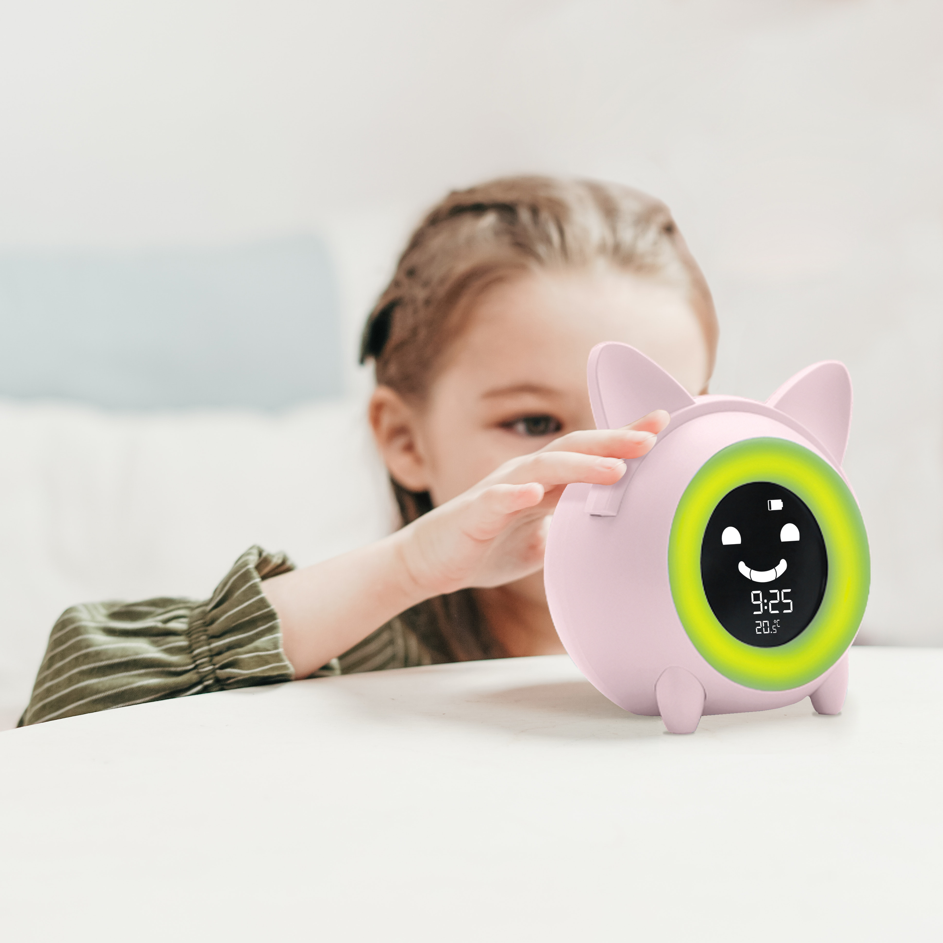 Un niño toca un despertador rosa con una pantalla sonriente. La hora es 9:25, la temperatura 20,5 grados.
