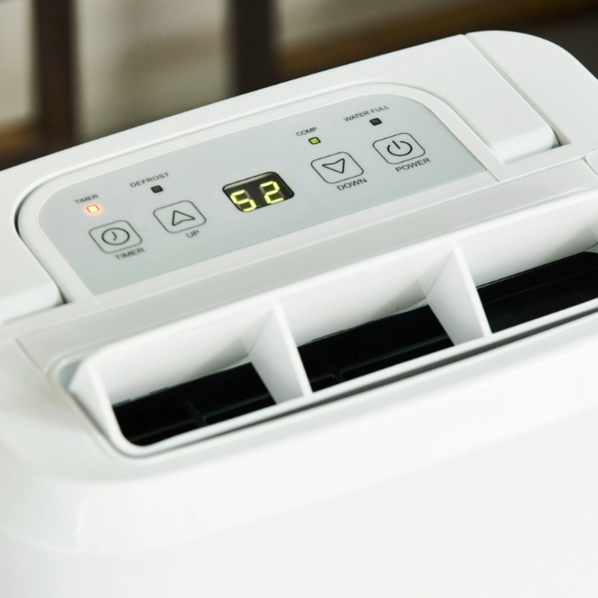 White dehumidifier with control panel showing a digital display reading 52. Buttons for timer, up, down, and power are visible.