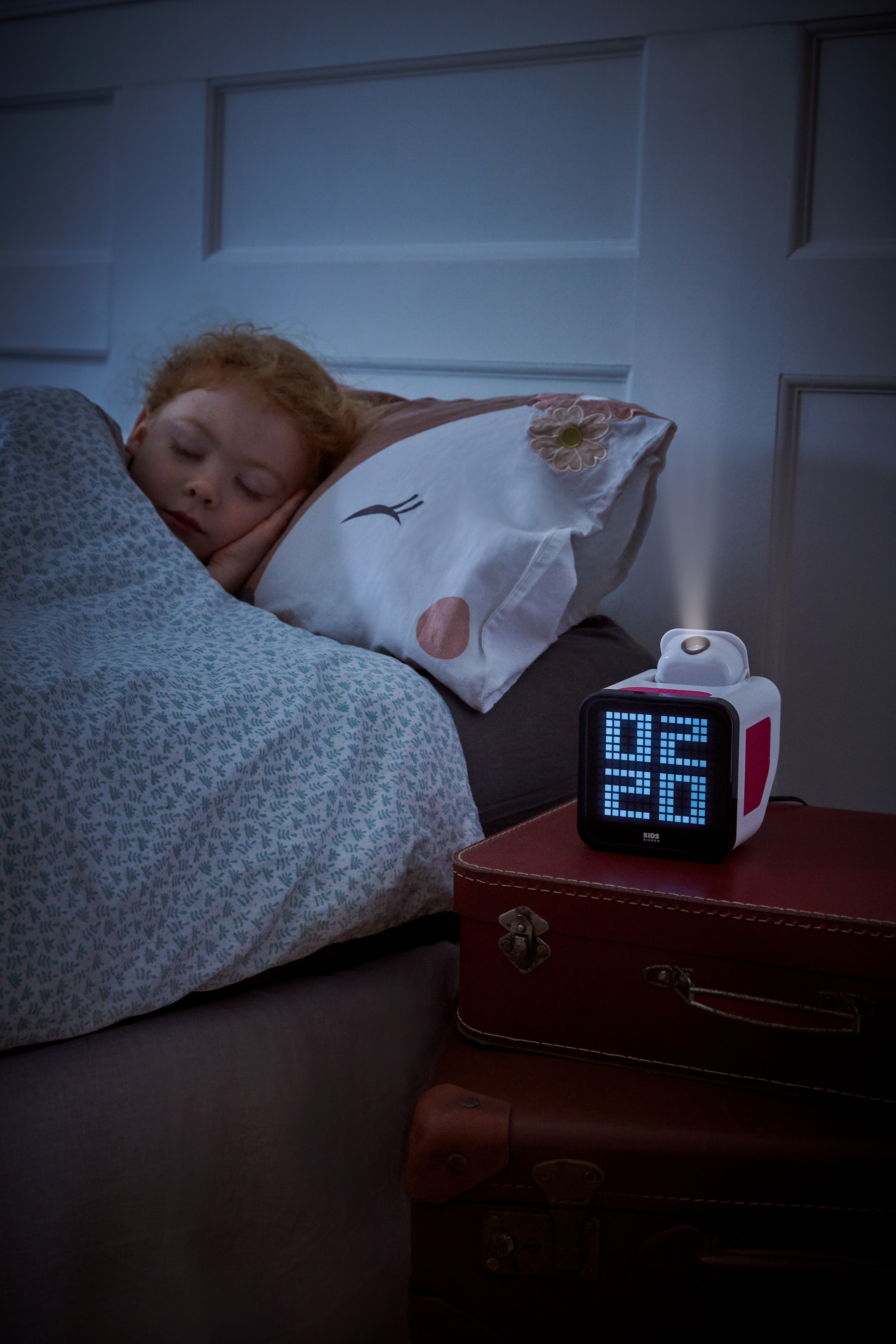 Un niño duerme en la cama. Un reloj muestra la hora. Maletas apiladas. Se ve una almohada de zorro. Habitación oscura.