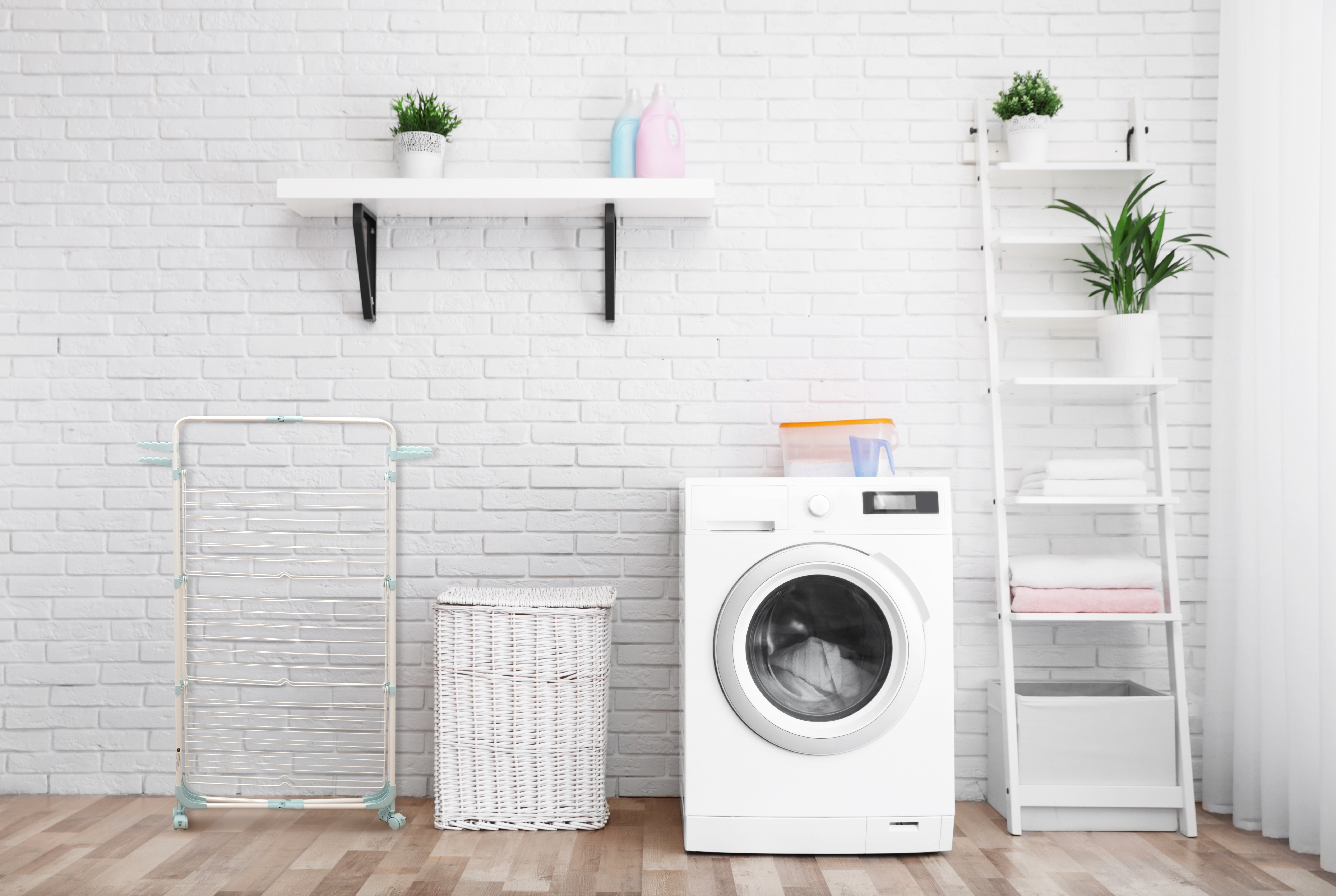 A laundry room with a washing machine, drying rack, and a wicker basket. There is also a ladder with plants and towels.